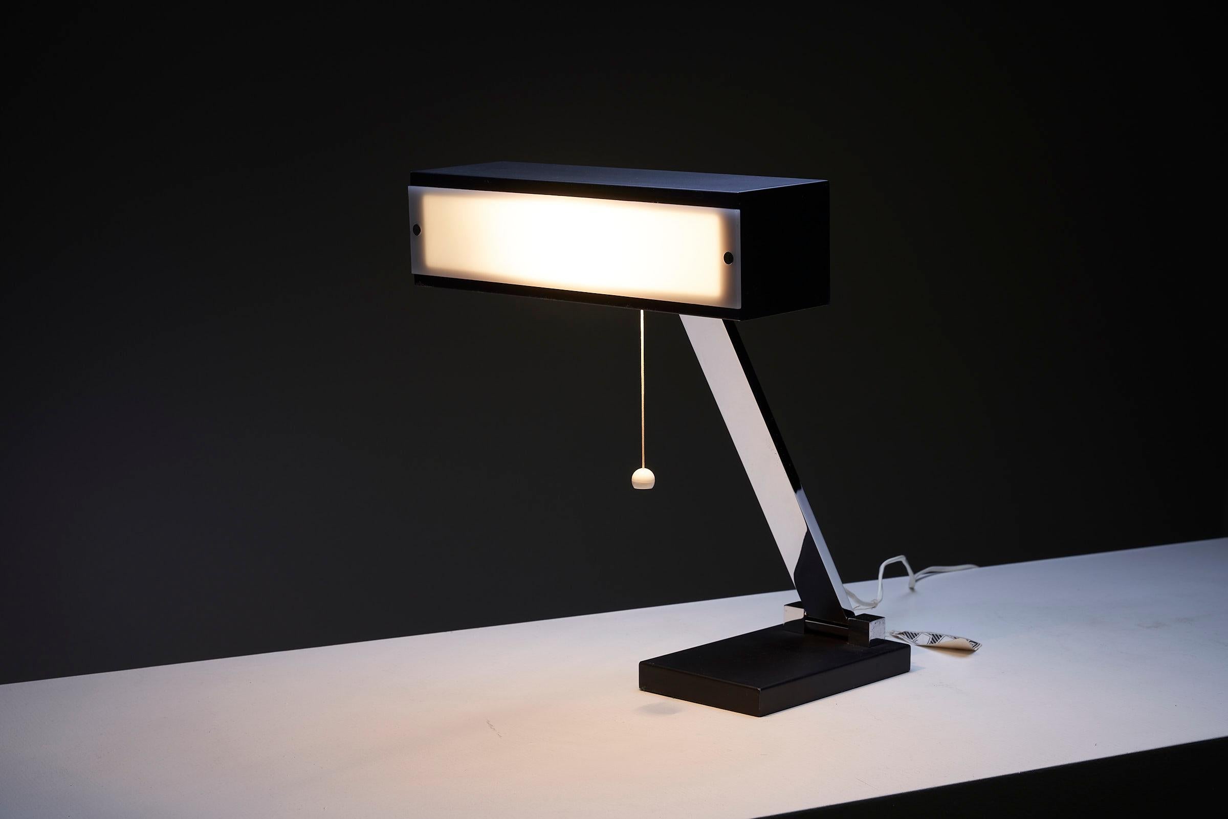 Table Lamp by Boulanger, Belgium, offers a sleek and modern lighting solution. The lamp features a black base and shade, connected by a chrome stem for added stability and visual appeal. The shade is equipped with a white plexi diffuser, allowing