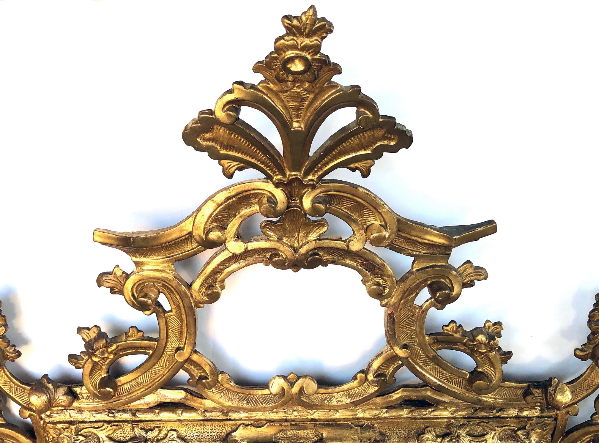 The exuberantly carved openwork crest composed of dramatic interlacing C-scroll motifs with floral and foliate elements cascading down the sides; all surrounding the original beveled mirror plate within a relief-carved molding