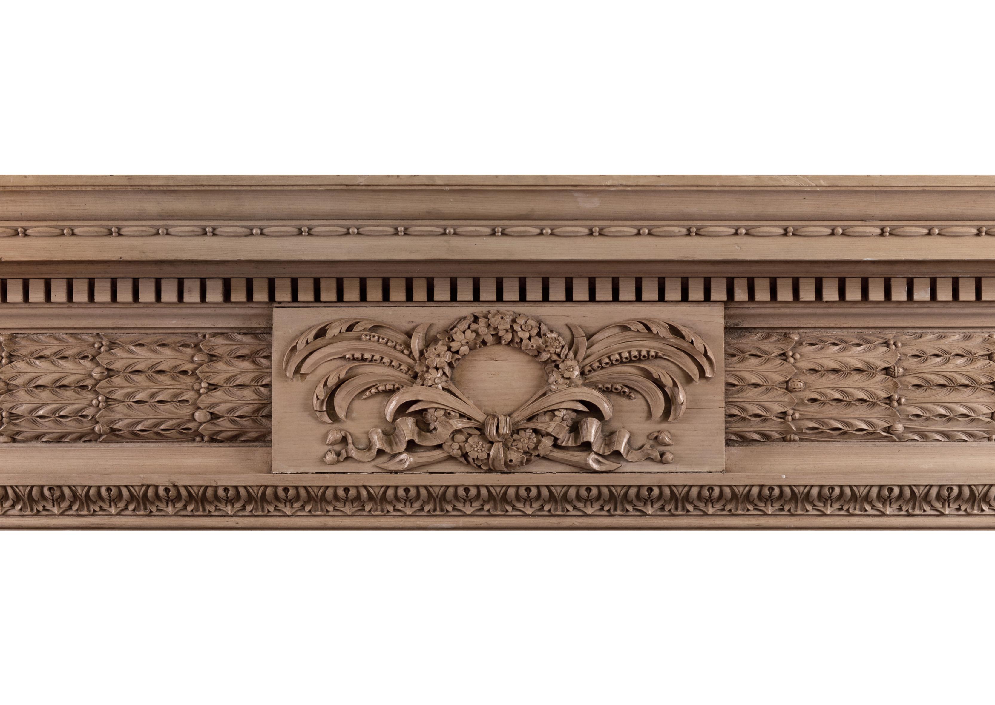 A well carved English pine fireplace. The intricate centre blocking featuring wreath, ribbons and foliage, flanked by barrelled frieze adorned with oak leaves. The jambs with acanthus leaves to inner moulding and carved belldrops. The shelf with