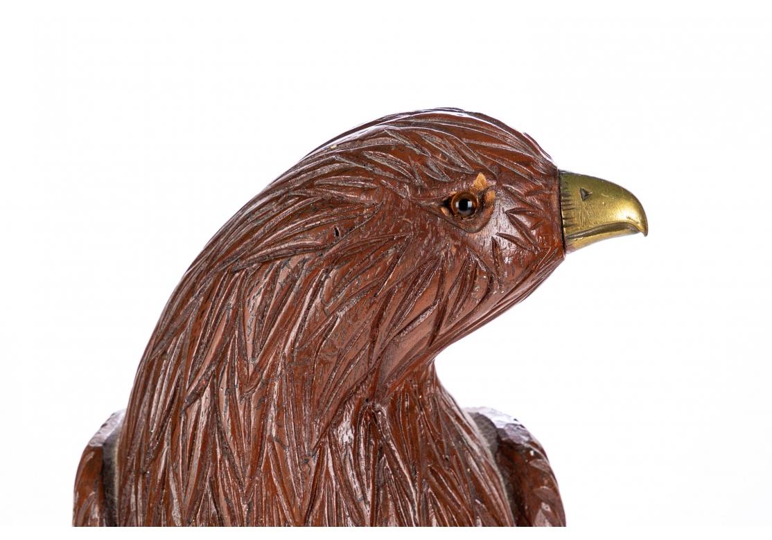 A carved and contrastingly stained wood eagle perched on a tree stump and surveying the surroundings. With life like feathers, brass beak and talons, and glass eyes. Mounted on a circular brass base. 
Measures: Height 24 1/2