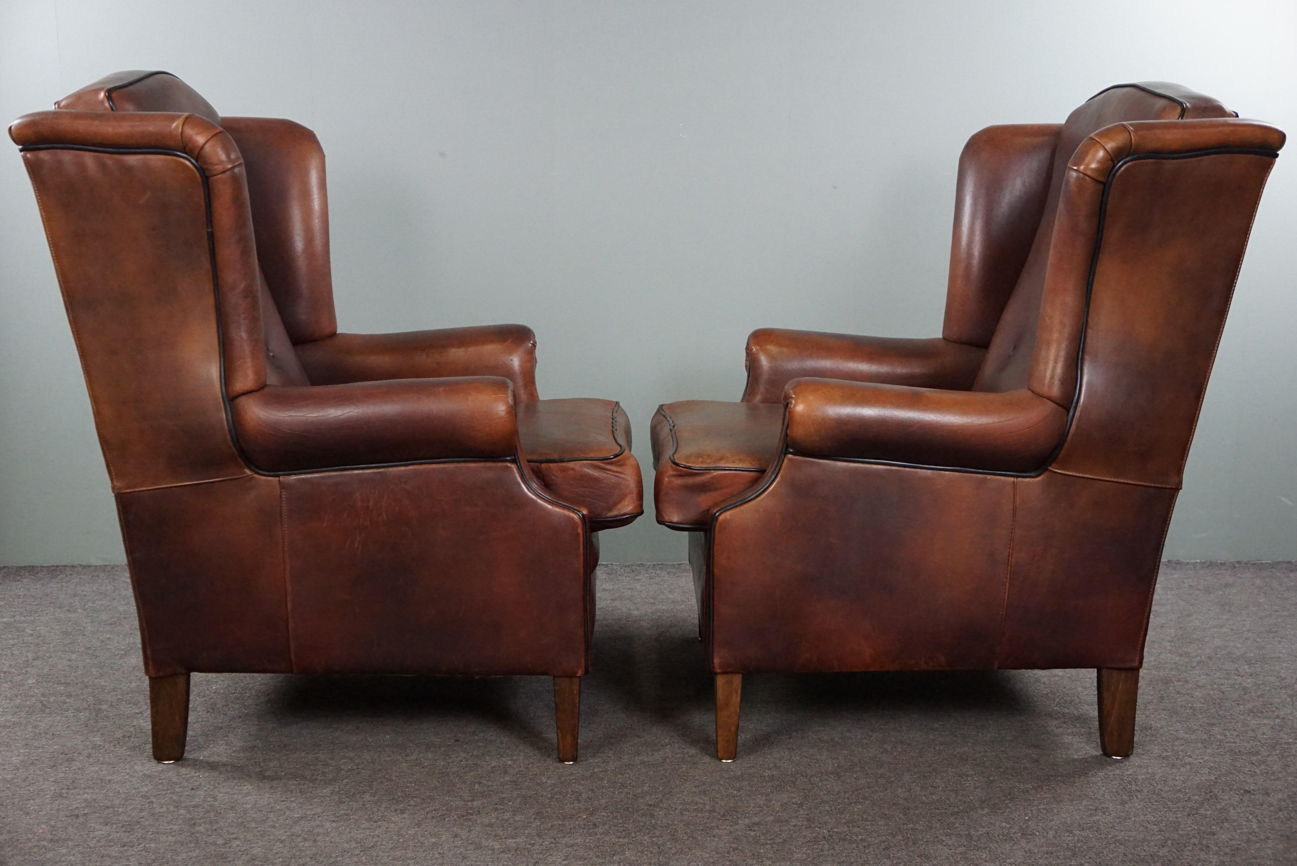 Offered is this well-fitting set of sheep leather wing chairs with charming compartments in the leather.

This comfortable and brightly colored set of two armchairs is a very good addition to almost any interior. The shape, the finish with the black