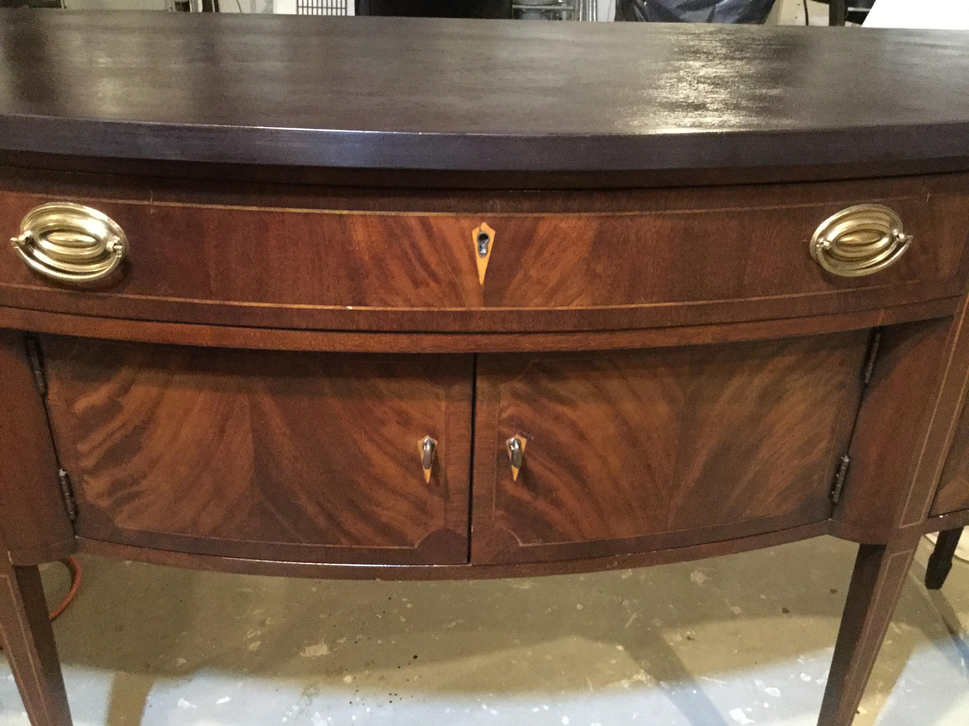 Made by Wellington Hall, this sideboard features lovely burled mahogany doors and drawers. There is satinwood banding on the tapered legs, and all original pulls and locks are intact. The top was recently refinished and is dark mahogany. The drawer