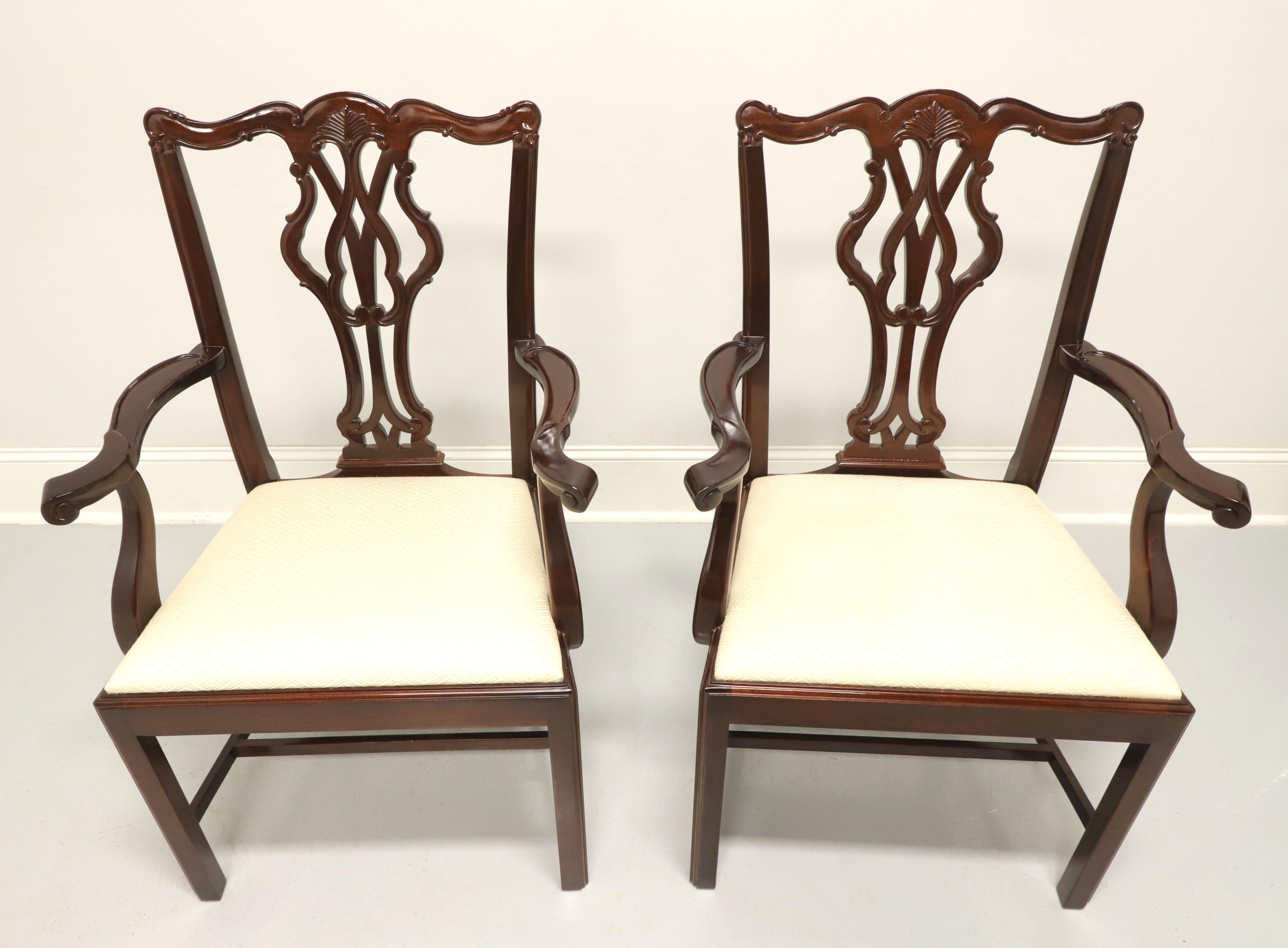 A pair of dining armchairs in the Chippendale style by Wellington Hall. Solid mahogany with carved crestrail, curved arms, carved seat back, cream color geometric pattern upholstered seat, straight legs and stretchers. Made in North Carolina, USA,