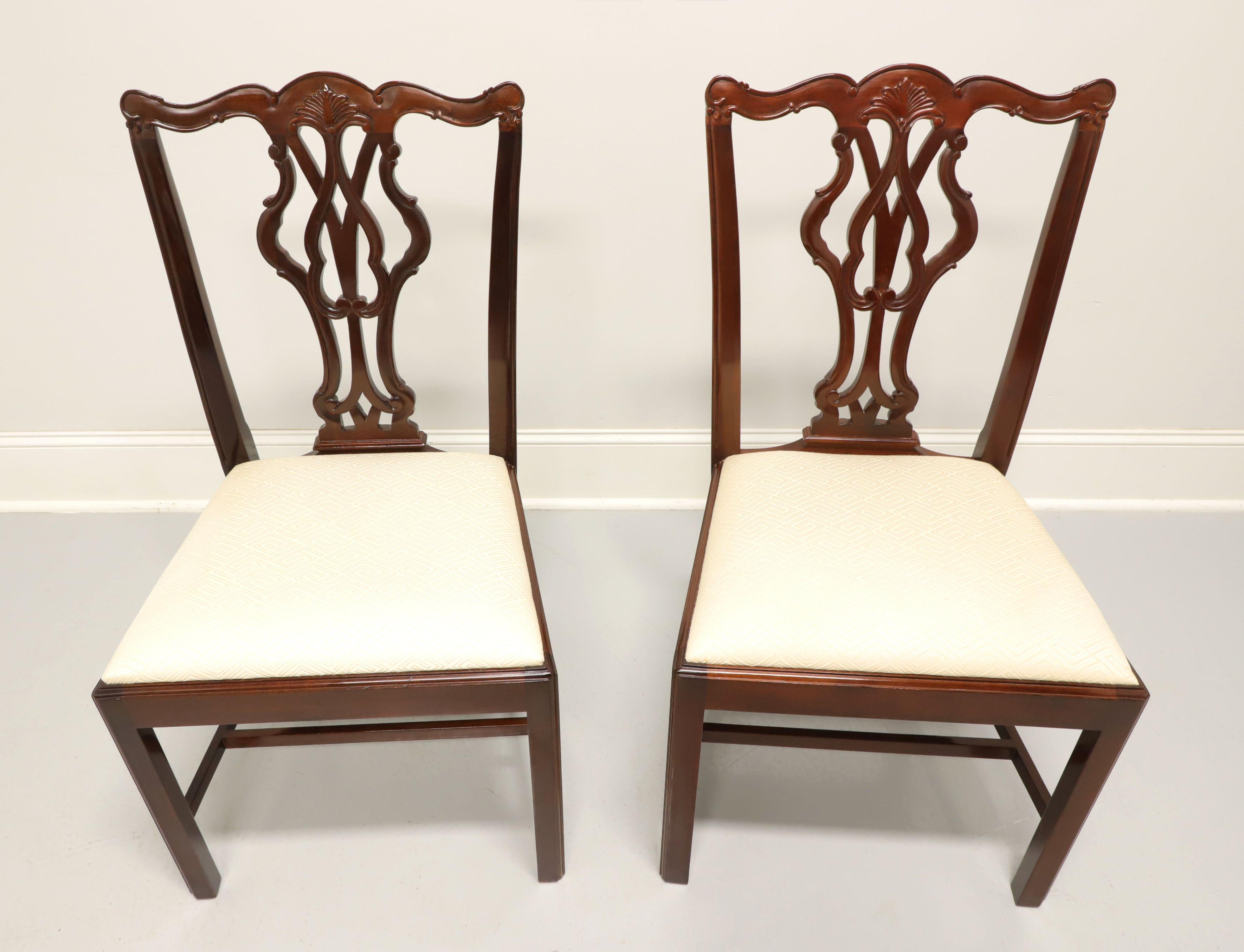 A pair of dining side chairs in the Chippendale style by Wellington Hall. Solid mahogany with carved crestrail, carved seat back, cream color geometric pattern upholstered seat, straight legs and stretchers. Made in North Carolina, USA, in the late