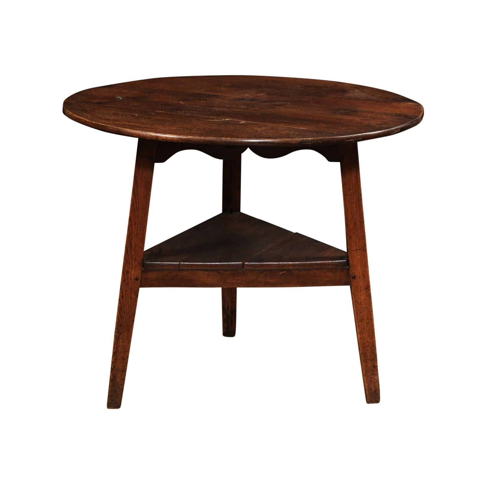 A Welsh chestnut cricket table from circa 1860 with circular top, carved scalloped apron on all sides and low triangular shelf. Immerse yourself in the timeless charm of this Welsh chestnut cricket table, hailing from circa 1860.

The table features