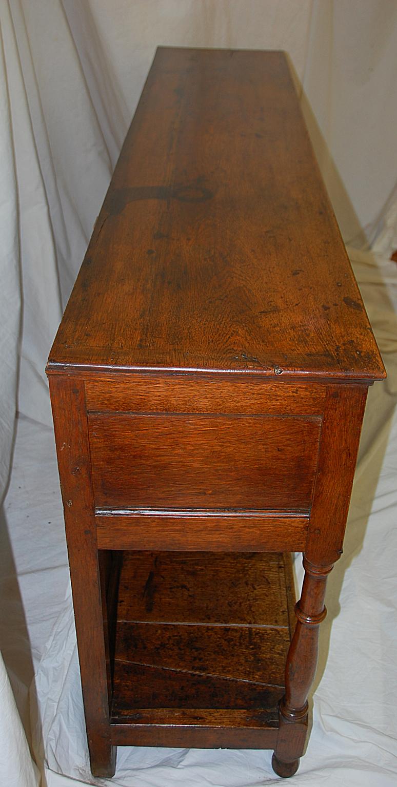 Welsh Georgian period oak three-drawer potboard low dresser from the Montgomeryshire district. This handsome 71 1/2 inch long dresser is unusual in having a full paneled back. The four turned pillars in the front separate the molded arches of the