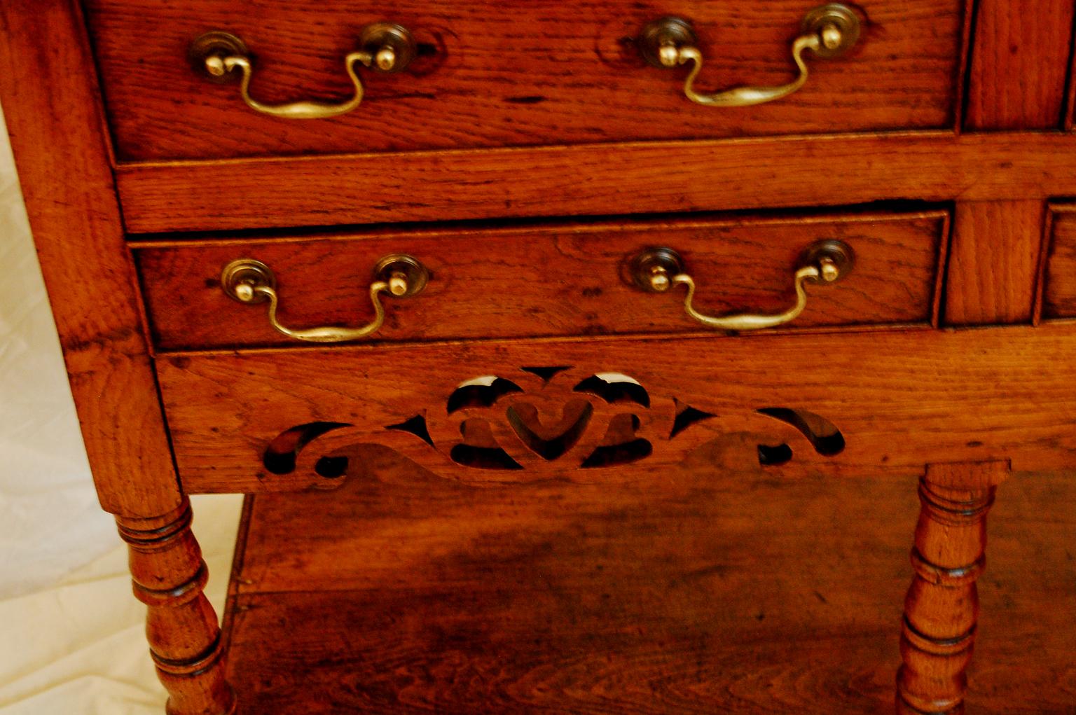 Welsh Georgian oak potboard dresser base with six drawers, turned legs, lower potboard shelf. This small dresser base, only five feet long, has an intricate pierced skirt which includes the heart motif. Very often that symbolizes that this was a
