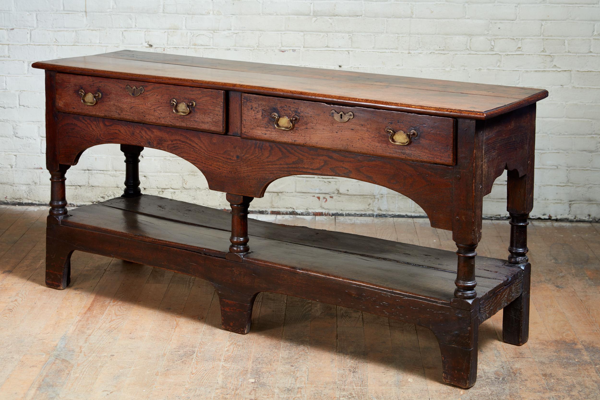 Fine Welsh 18th century low dresser of sculptural form, the two plank top with thumb molded edge over two drawers with double arched apron below and standing on balustrade turned legs having pot board and standing on bracket feet, the whole