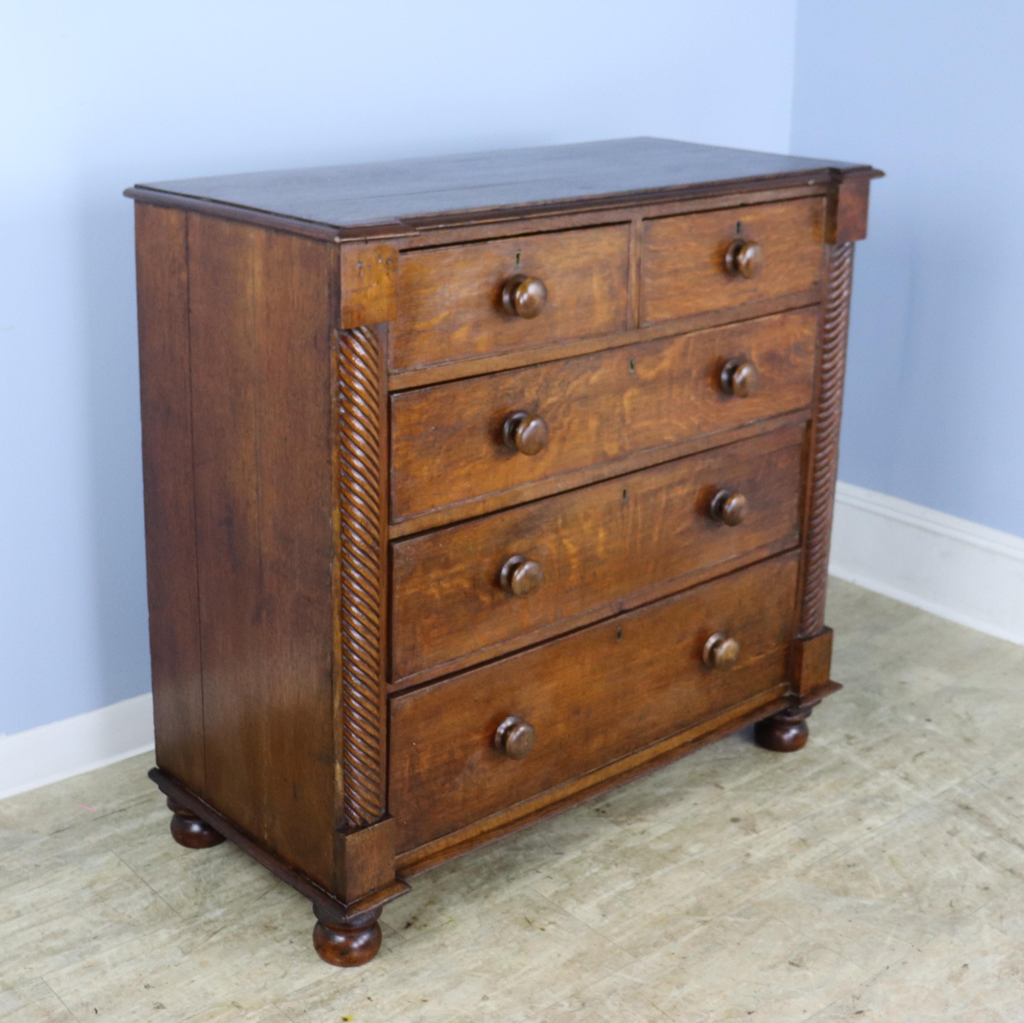 A charming oak chest of drawers in well grained and colored oak.  The twist columns at either side add an eye catching design note, as do the bun feet.  This piece is in good antique condition for it's age and use.