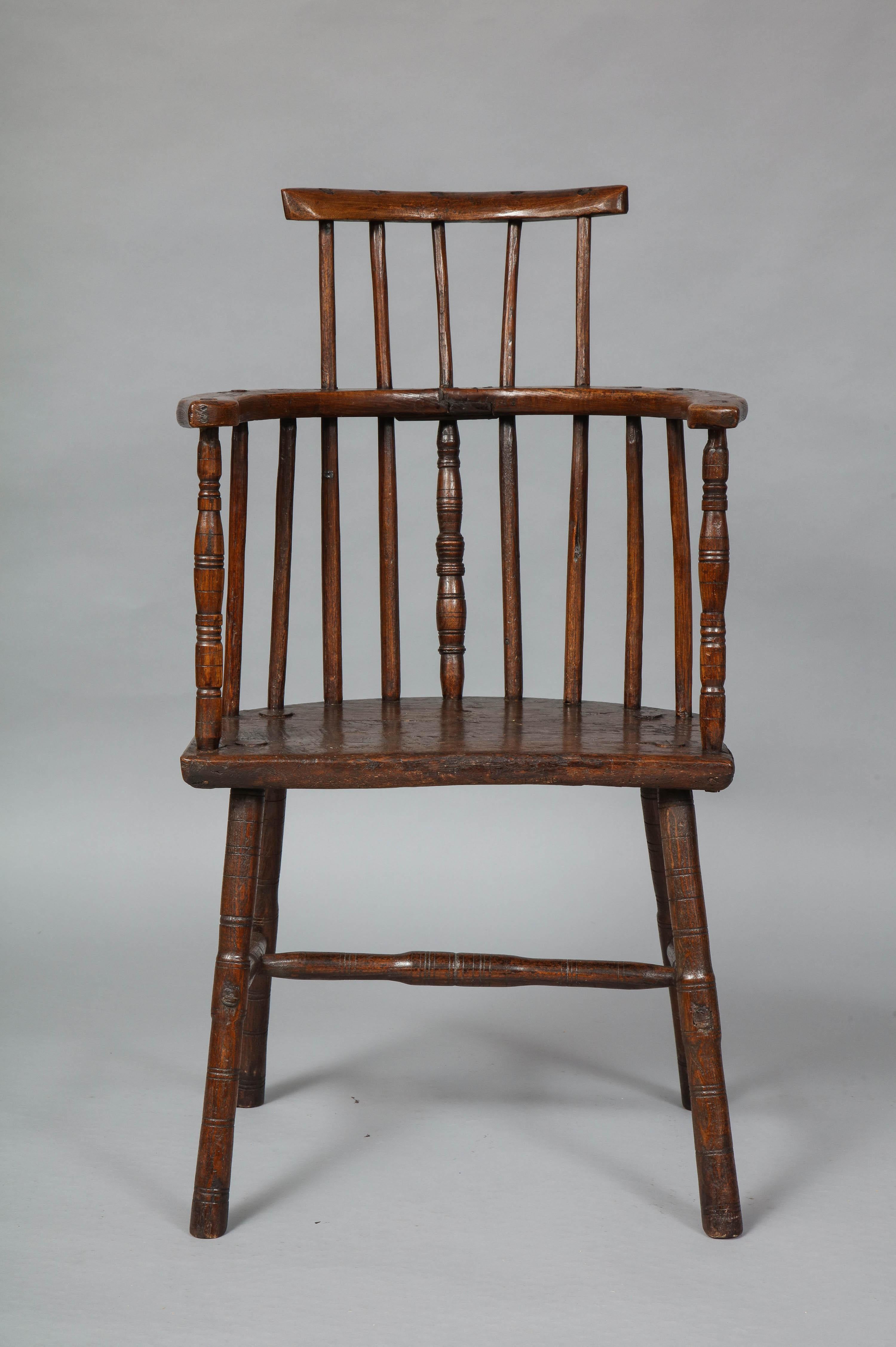 Unusual early 19th century Welsh oak diminutive windsor chair having simple comb back, over spoke shaved spindles and turned center and arm supports, over two plank oak seat and with pole lathe turned legs and 