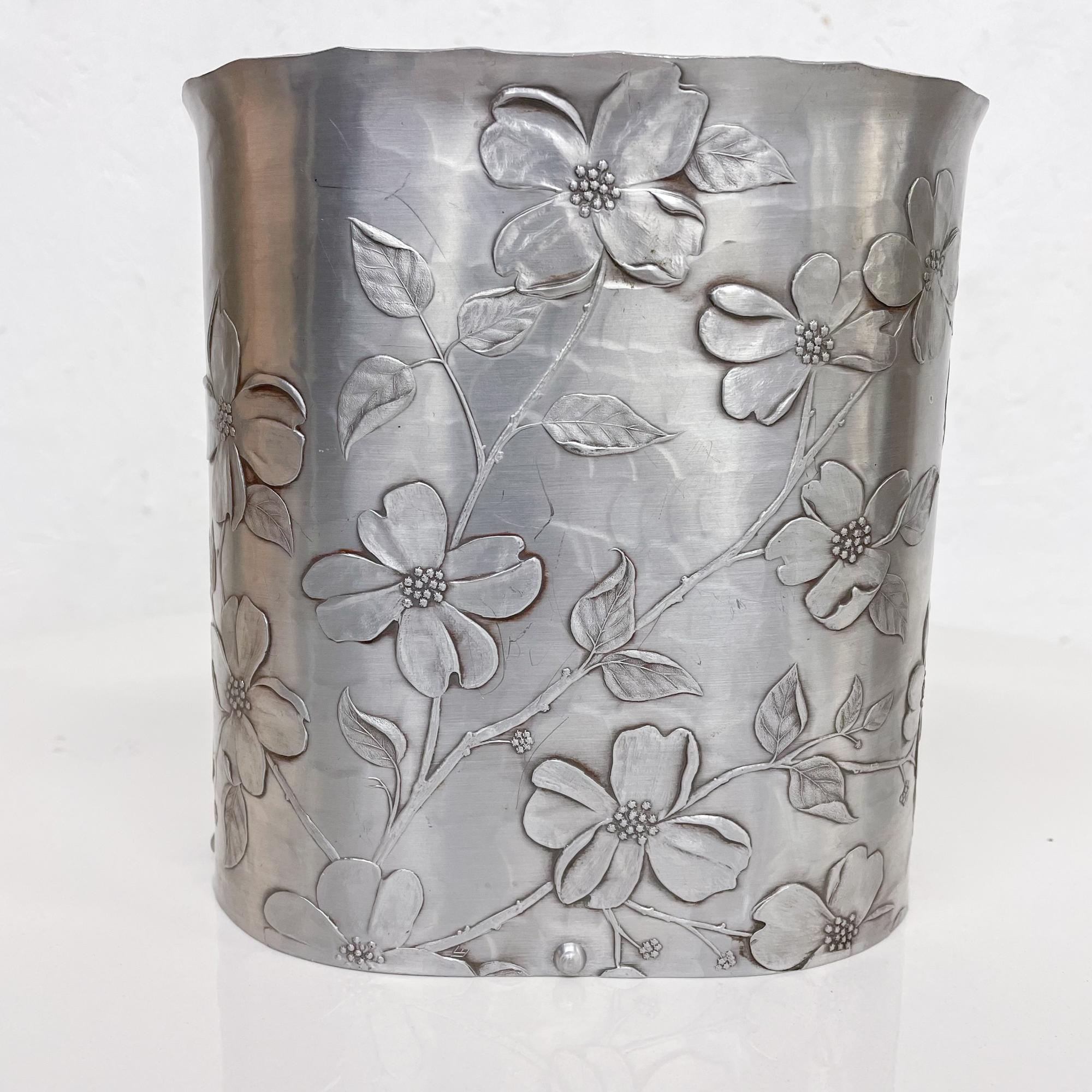 Waste Basket
Wendell August Forge Pretty Petite handmade wastebasket trashcan dogwood motif in hammered riveted art iron aluminum 1960s.
Designed by Wendell August.
Short version in oval shape. 
Measures: 6.88h x 6.75w x 4.5 inches
Maker