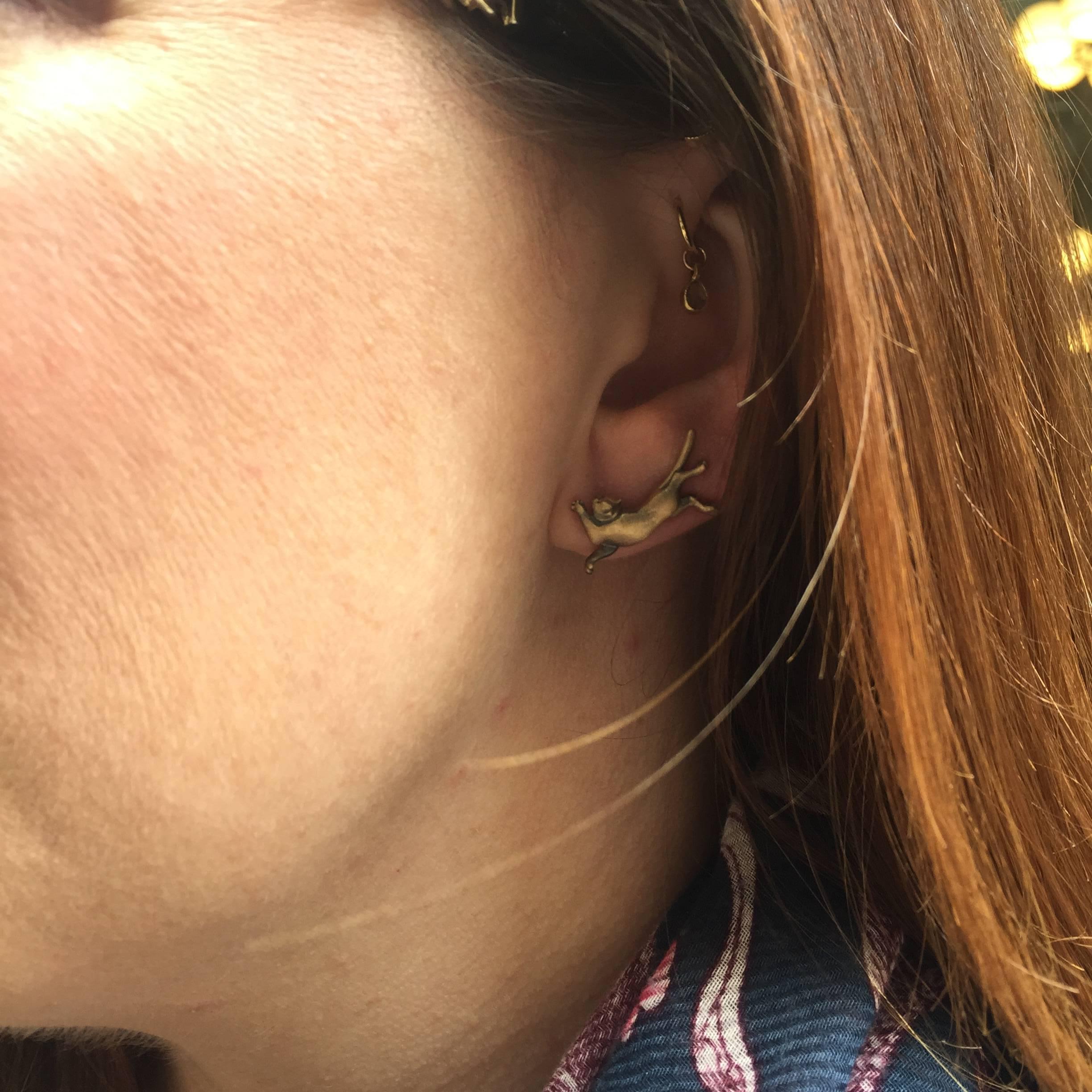 18K Gelbgold, satiniert.
Der Draht wird durch das Ohrpiercing geführt; dann dreht die Trägerin oder der Träger das Stück so, dass die Katze auf dem Ohrläppchen ruht.
Limitierte Auflage: Eines von nur zwei hergestellten Paaren.

Wendy Brandes Gold