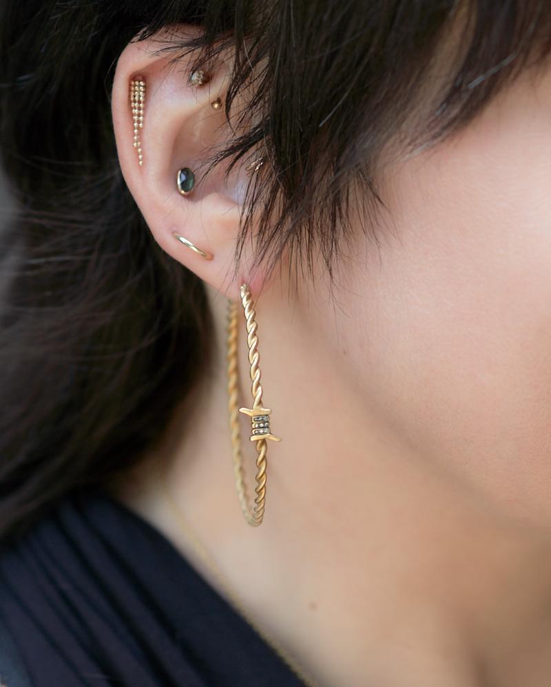 These hoop earrings have a twisting barbed wire motif for a subtle punk-rock vibe.

18K yellow gold, satin finish.
18 diamond rounds totaling 0.05 carats (E/F, VS1/VS2).
2