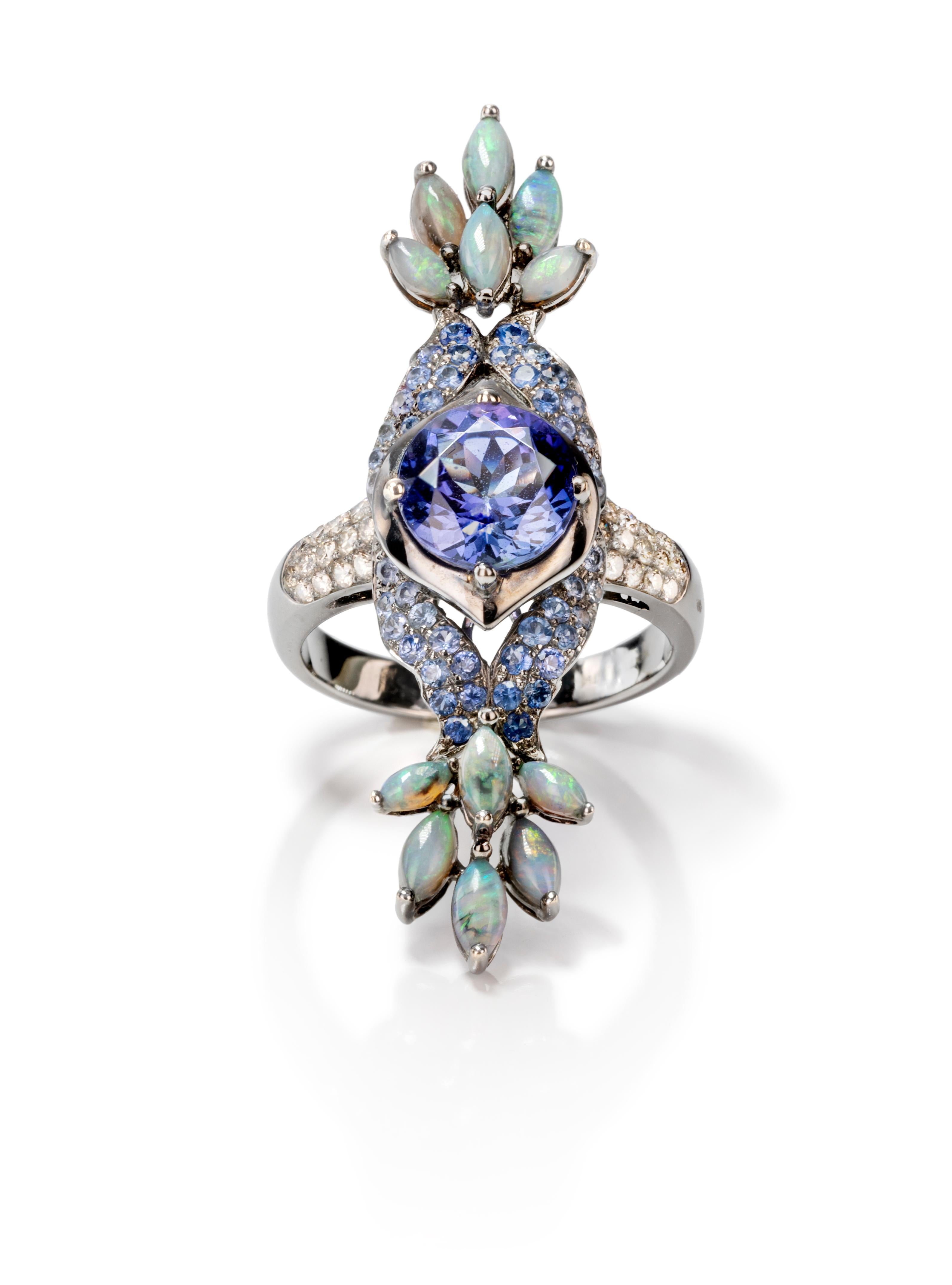 As the peacock displays its feathers in a flourish of color, the Tanzanite and Opal Peacock Ring dazzles with sparkle and flare. A tanzanite stone sits atop an 18k white gold and diamond band and is surrounded by a shell of blue sapphires. Tails of