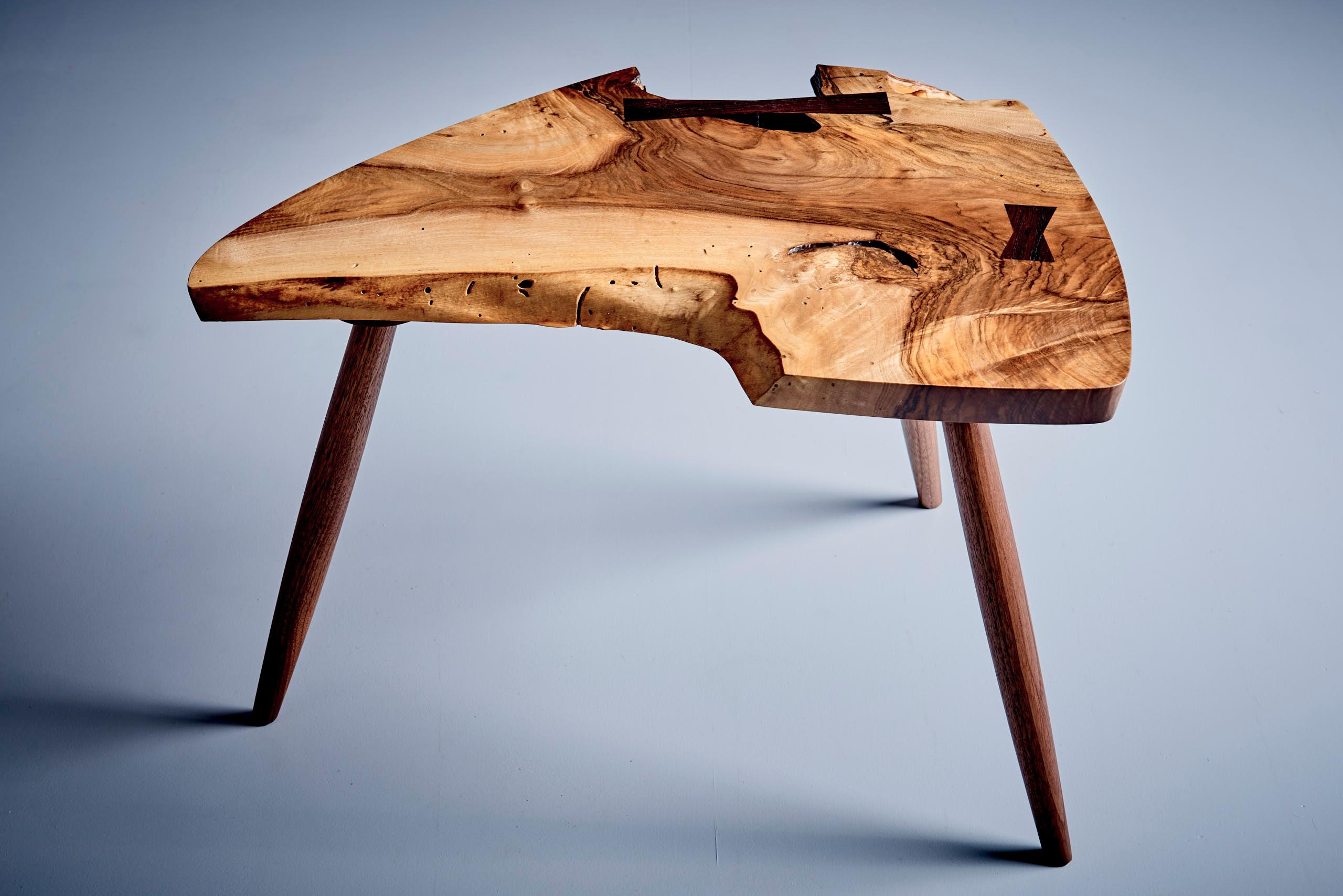 La table W36 Wepman est une pièce unique fabriquée à la main en noyer anglais, avec un aubier large, un design à bords libres et un grain figuré saisissant. Les fissures naturelles du bois sont stabilisées par deux papillons de bois, mêlant ainsi