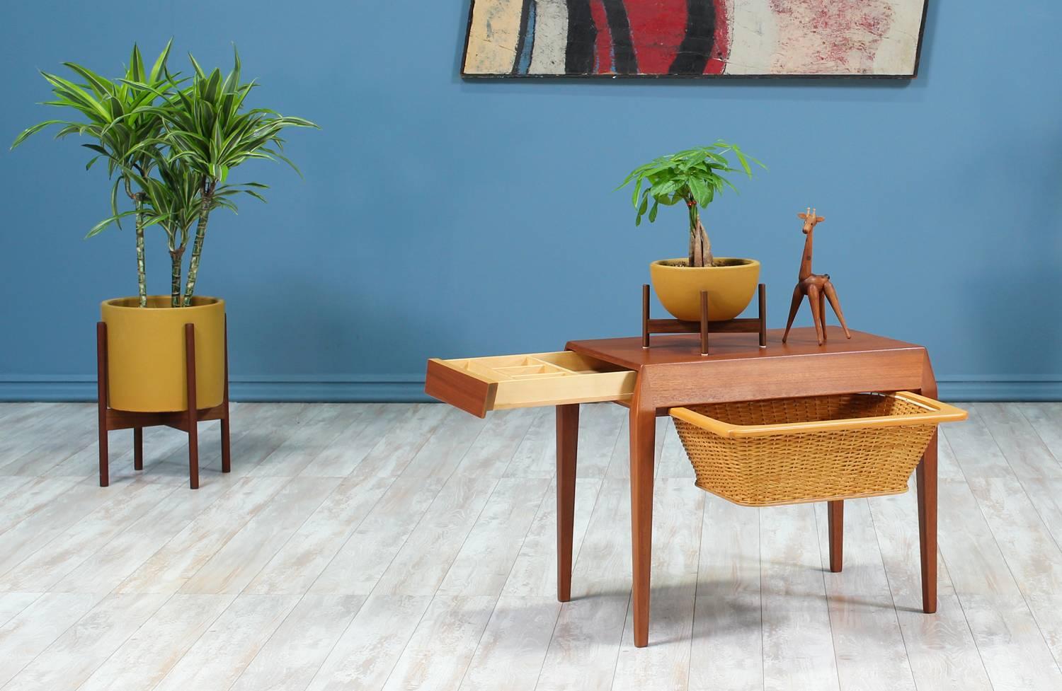 Sewing Table designed by Werner Fredriksen for Eric Gustavsson Möbelfabrik in Sweden circa 1960’s. This Swedish Modern design features a teak wood frame with beveled edges and its original pull-out wicker basket. The left side features a