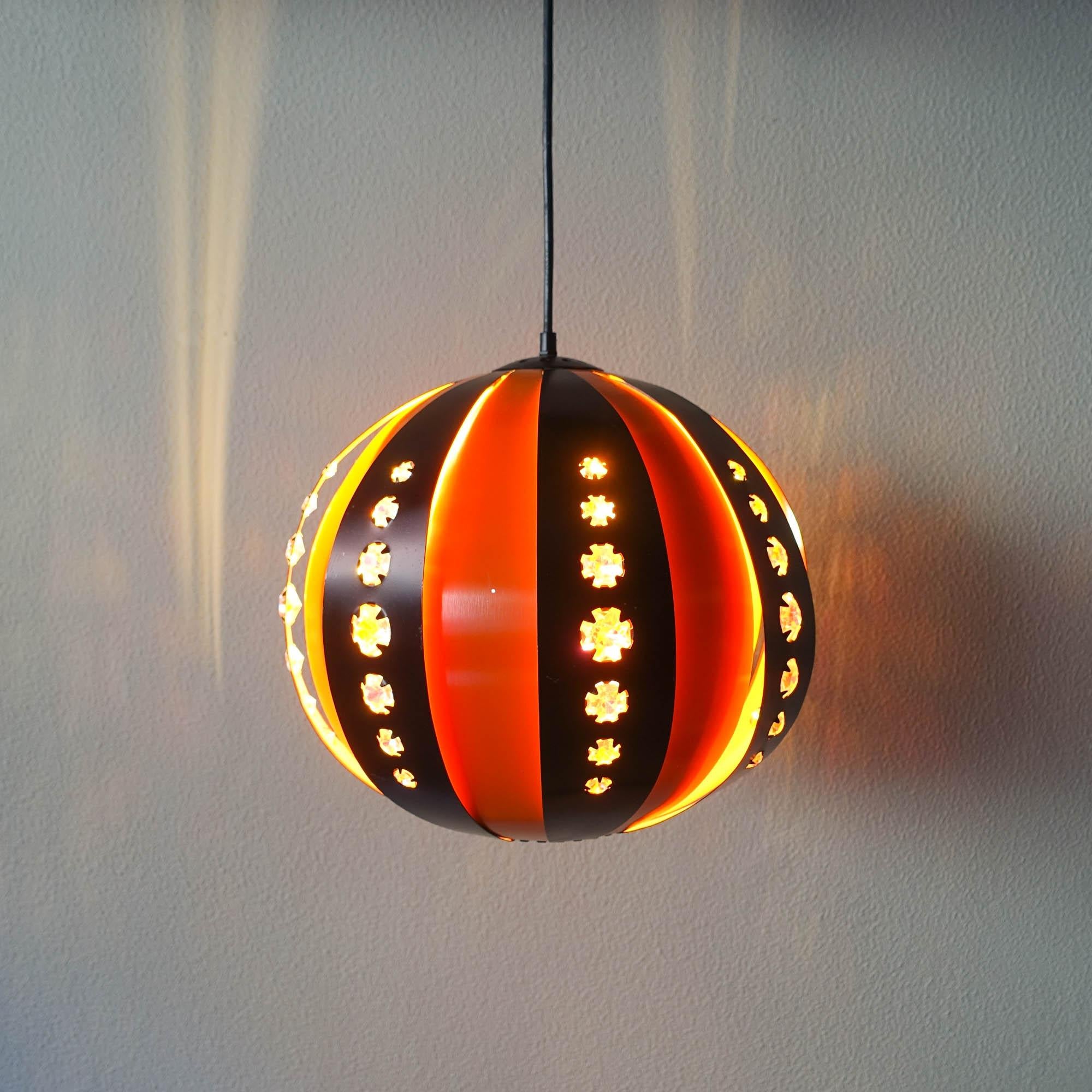 This pendant lamp was designed by Werner Schou for Coronell Elektro, in Denmark during the 1907's. The lamp is made of aluminum in black and orange, with glass inserts in the black part. These glasses reflect the light and helps to spread a warm
