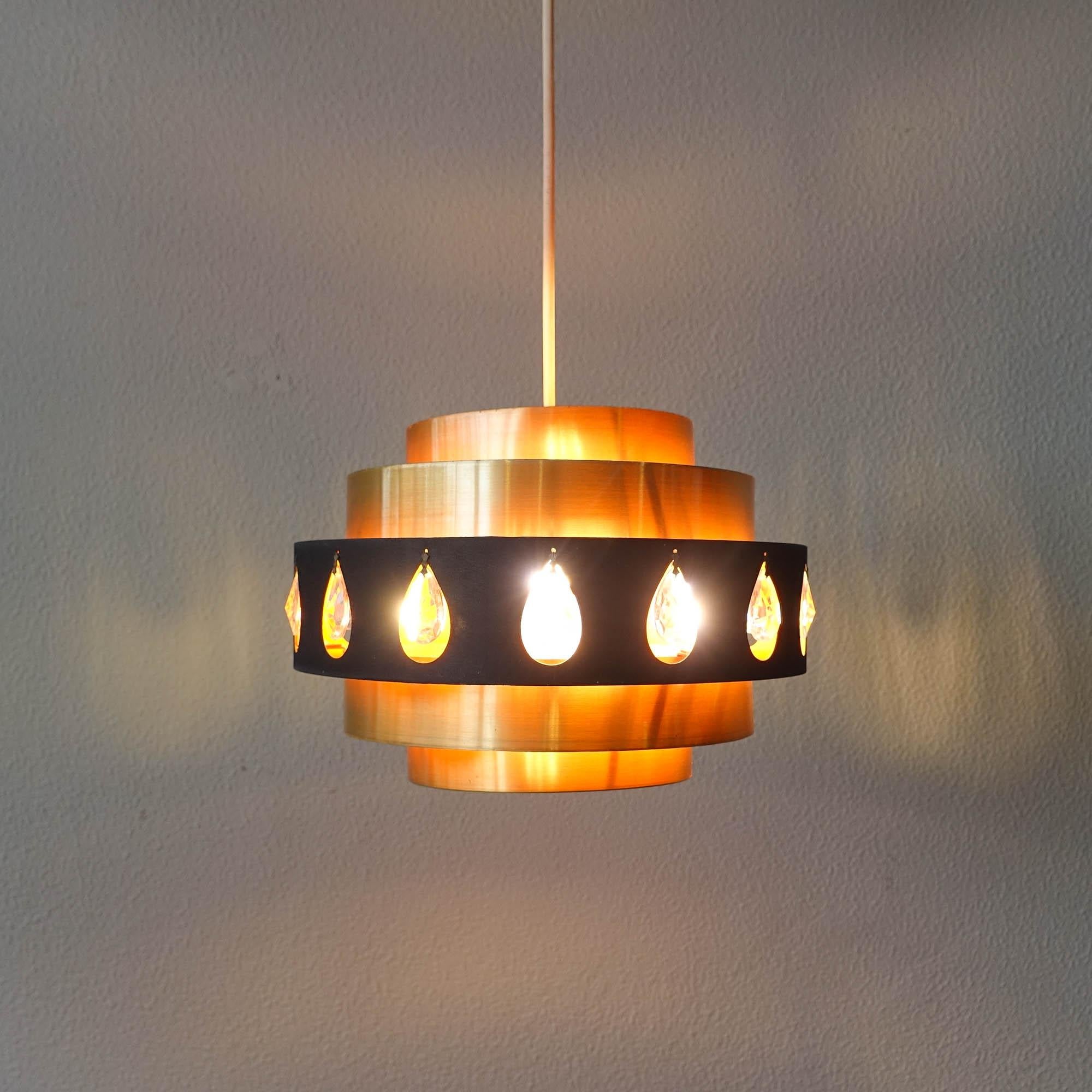 This pendant lamp was designed by Werner Schou for Coronell Elektro, in Denmark during the 1970's. The lamp is made of aluminum in black and gold, with glass inserts in the black part. These glasses along with the orange paint inside reflect the