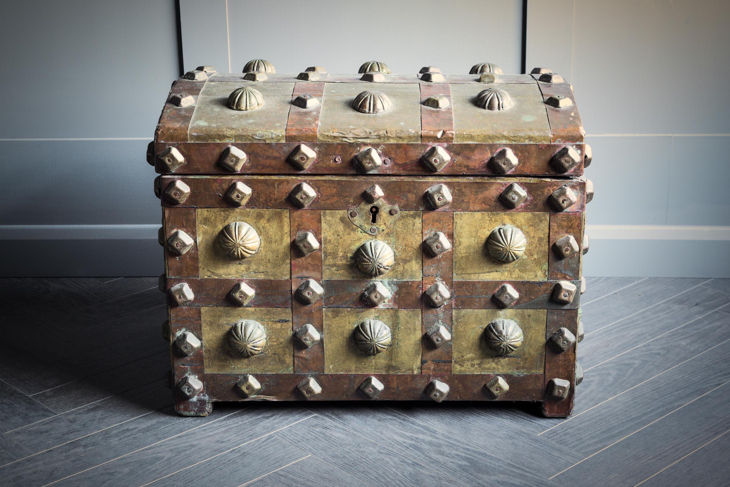 Eine mittelgroße Berber-Aussteuertruhe westafrikanischer Herkunft, deren Außenseite mit Metallzwiebeln kunstvoll verziert ist. Der Deckel lässt sich an zwei Metallscharnieren öffnen und gibt den Blick auf ein Mehrzweckfach im Inneren frei. Diese