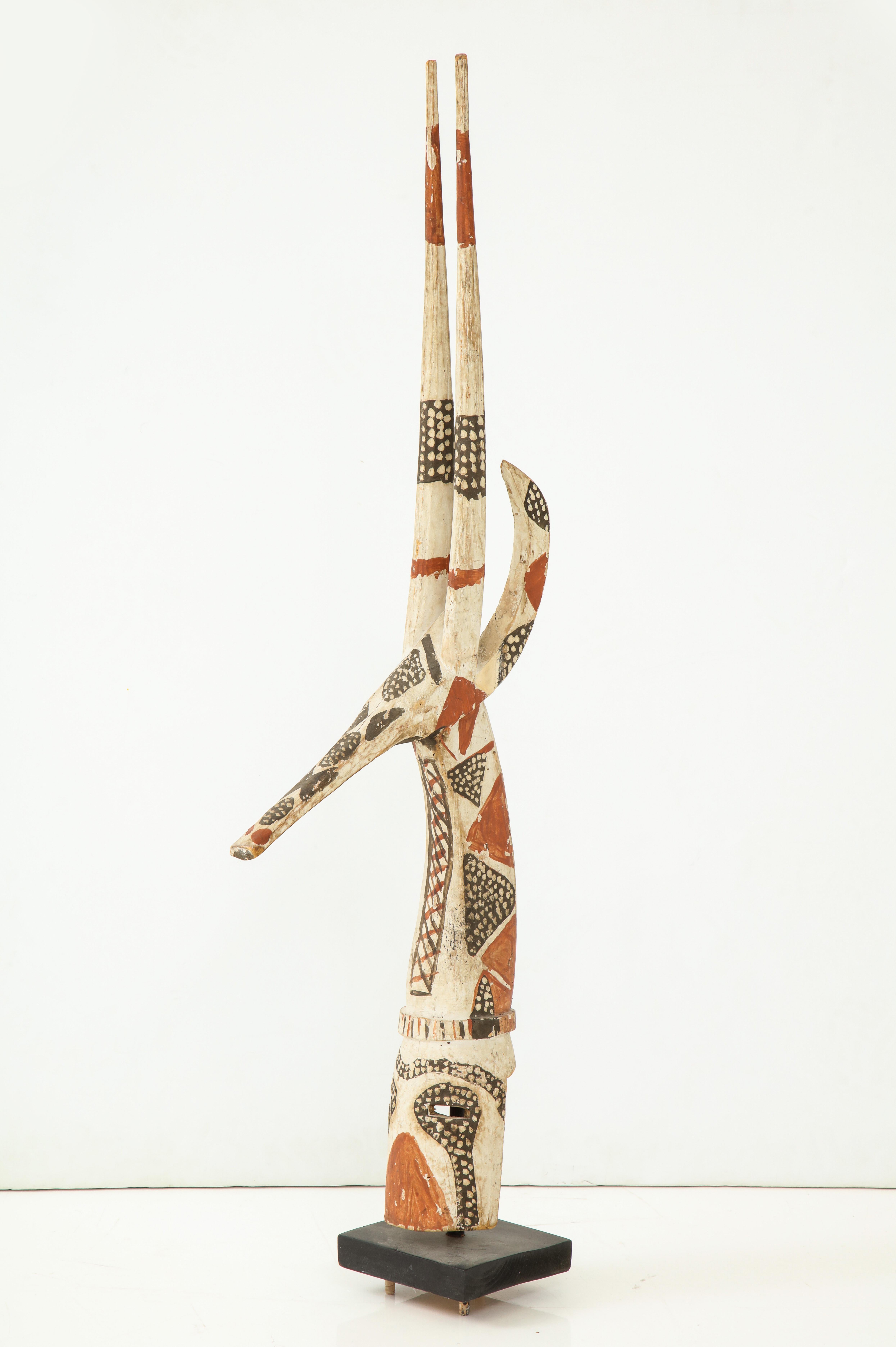 Carved wooden fertility dance mask; painted and decorated with seed motifs, the sculpture in the shape of a giraffe, with cutout eye holes and back for the face; mounted on a square wooden plinth.
West Africa, circa 1960s.
Size: 43 1/2