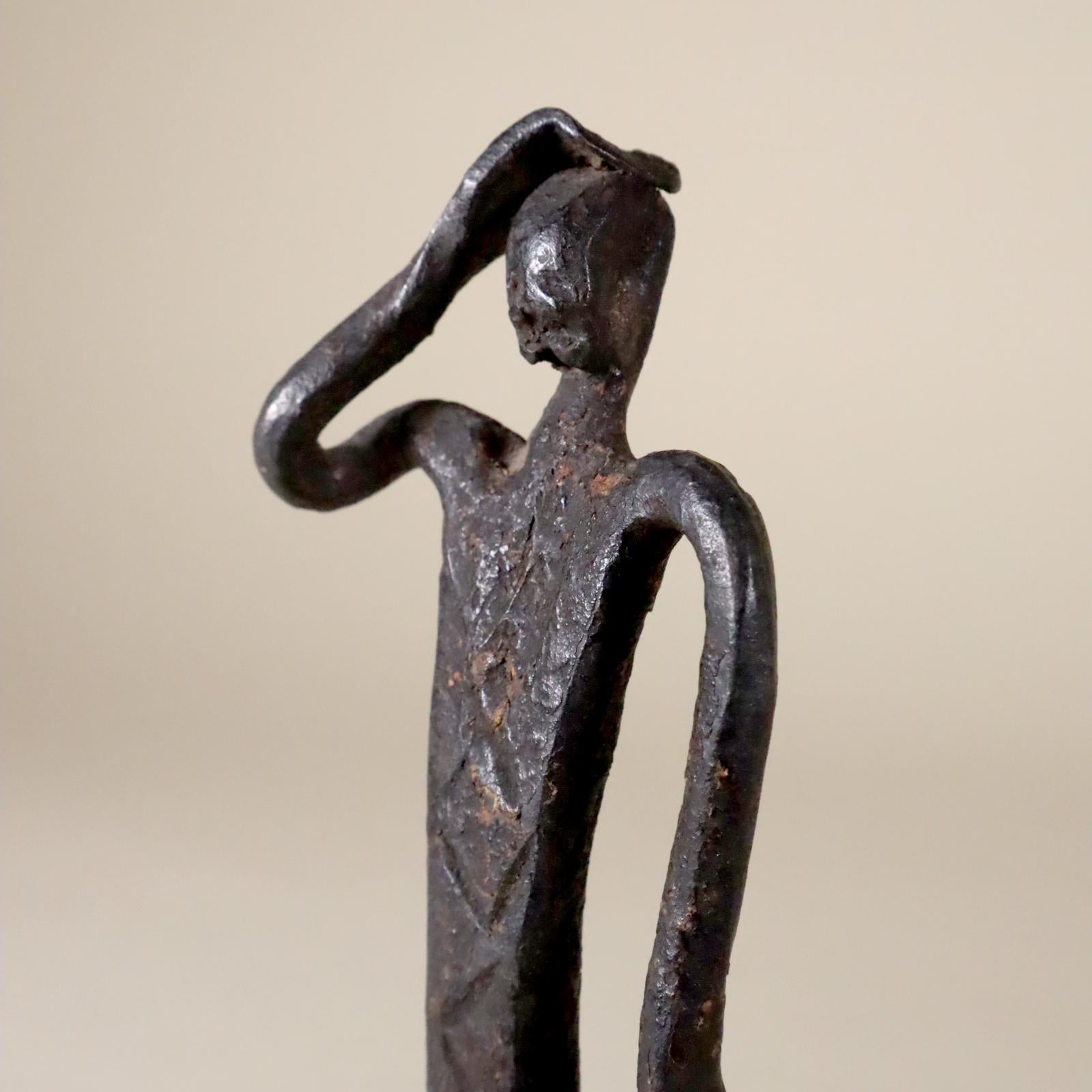 A finely rendered and expressive iron figure from West Africa, not sure where, most likely from either the Dogon or the Bamana (var. Bambara) people of Mali, West Africa. A kneeling figure with right hand raised to head. Engraved zigzag lines down