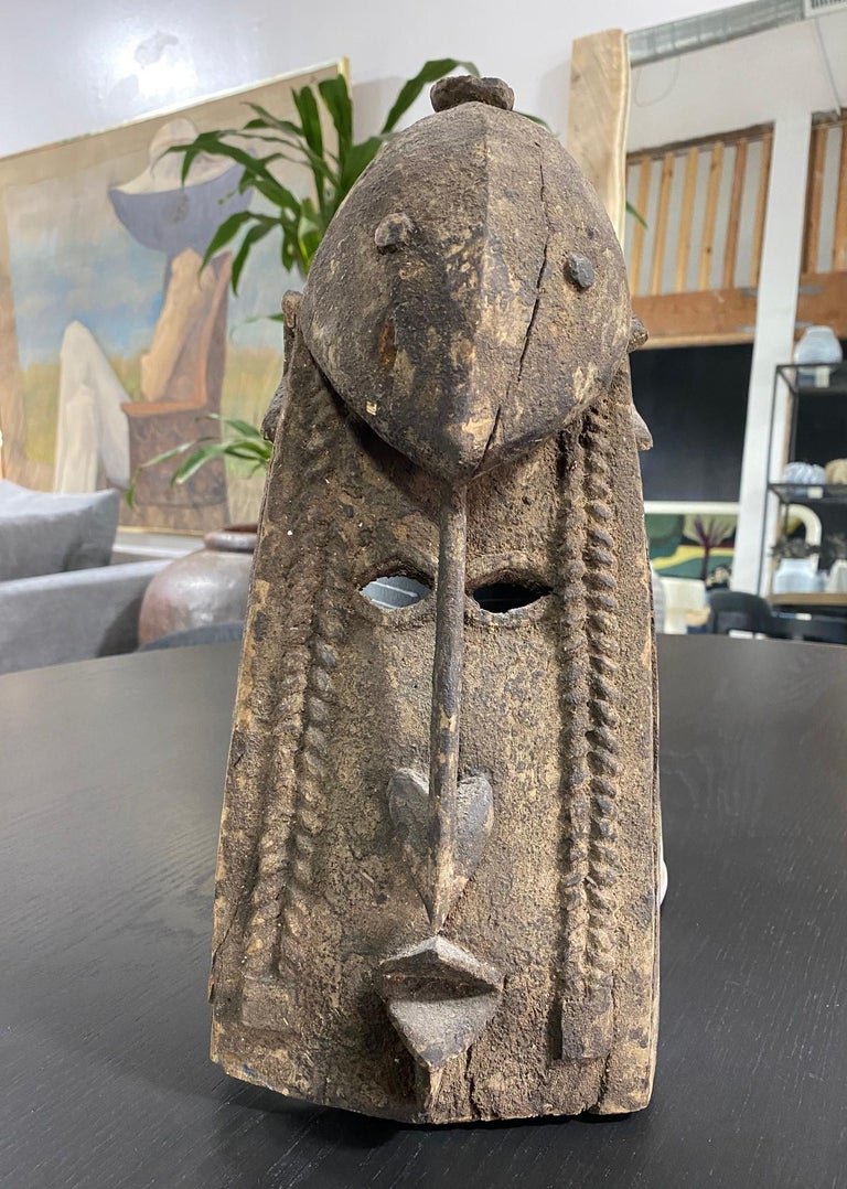 A wonderful, decorative African mask with elongated features, detailed facial markings, and some sort of anthropomorphic animal sitting at the top of the head. Has a beautiful patina and encrusted finish with clear age. Likely made to be worn during
