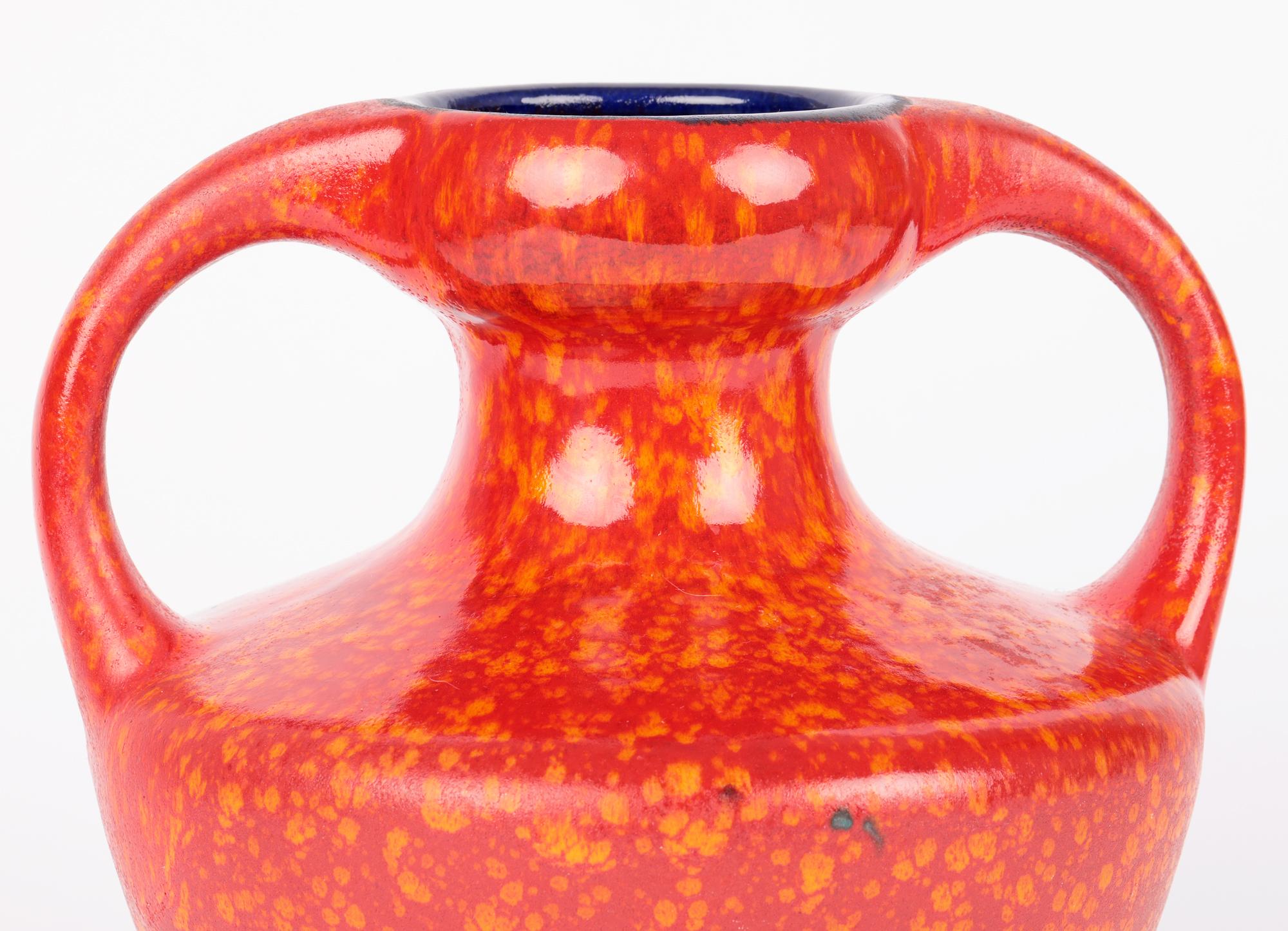 A very stylish West German midcentury mottle red and orange glazed twin handle art pottery vase. The red stoneware vase stands on a narrow round unglazed foot and is of wide round bulbous shape with a narrow pinched neck and raised wide shallow bowl