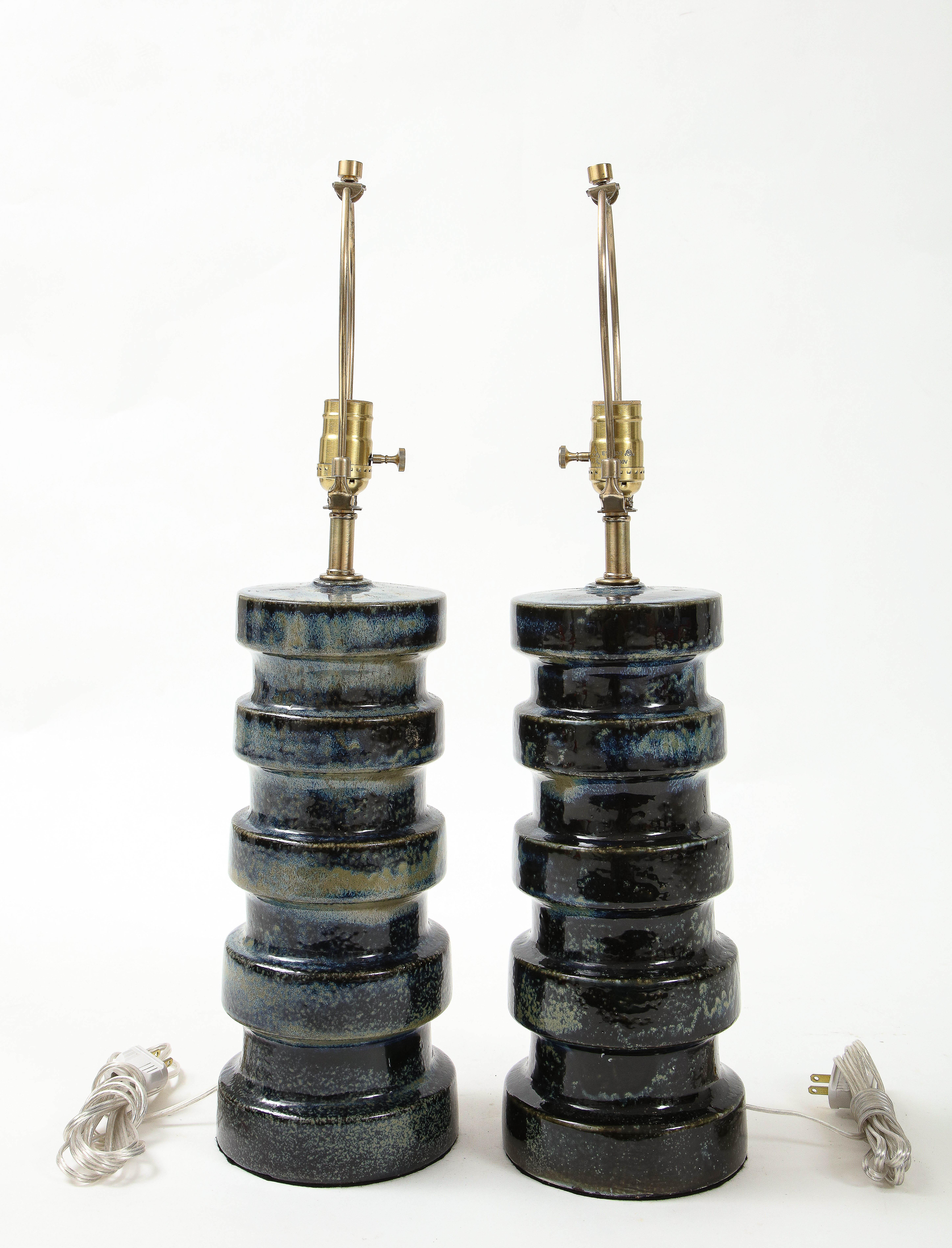 Pair of West German pottery lamps featuring striated colors of dark blue and tan colors. Lamps have been rewired to US standards using brass hardware, 100W max bulbs.