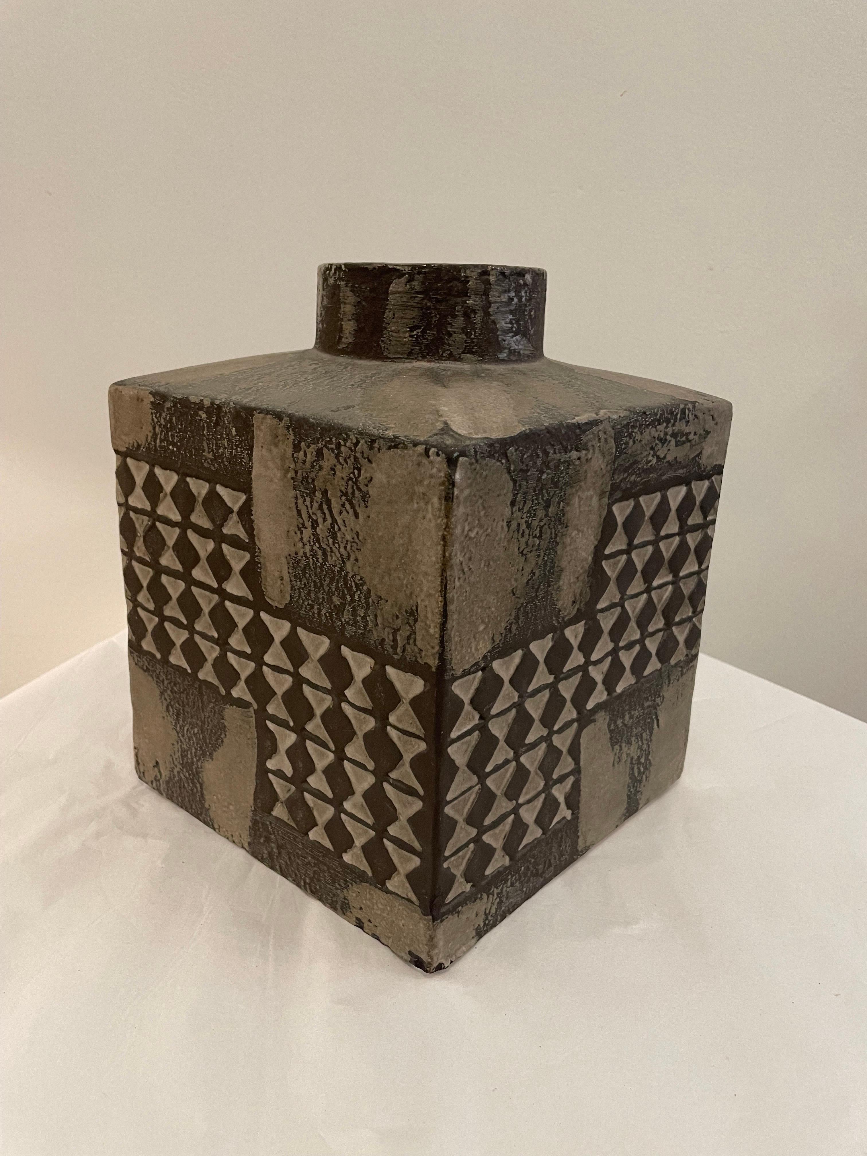 Merveilleux vase carré en finition texturée gris lave aux formes géométriques et de style.