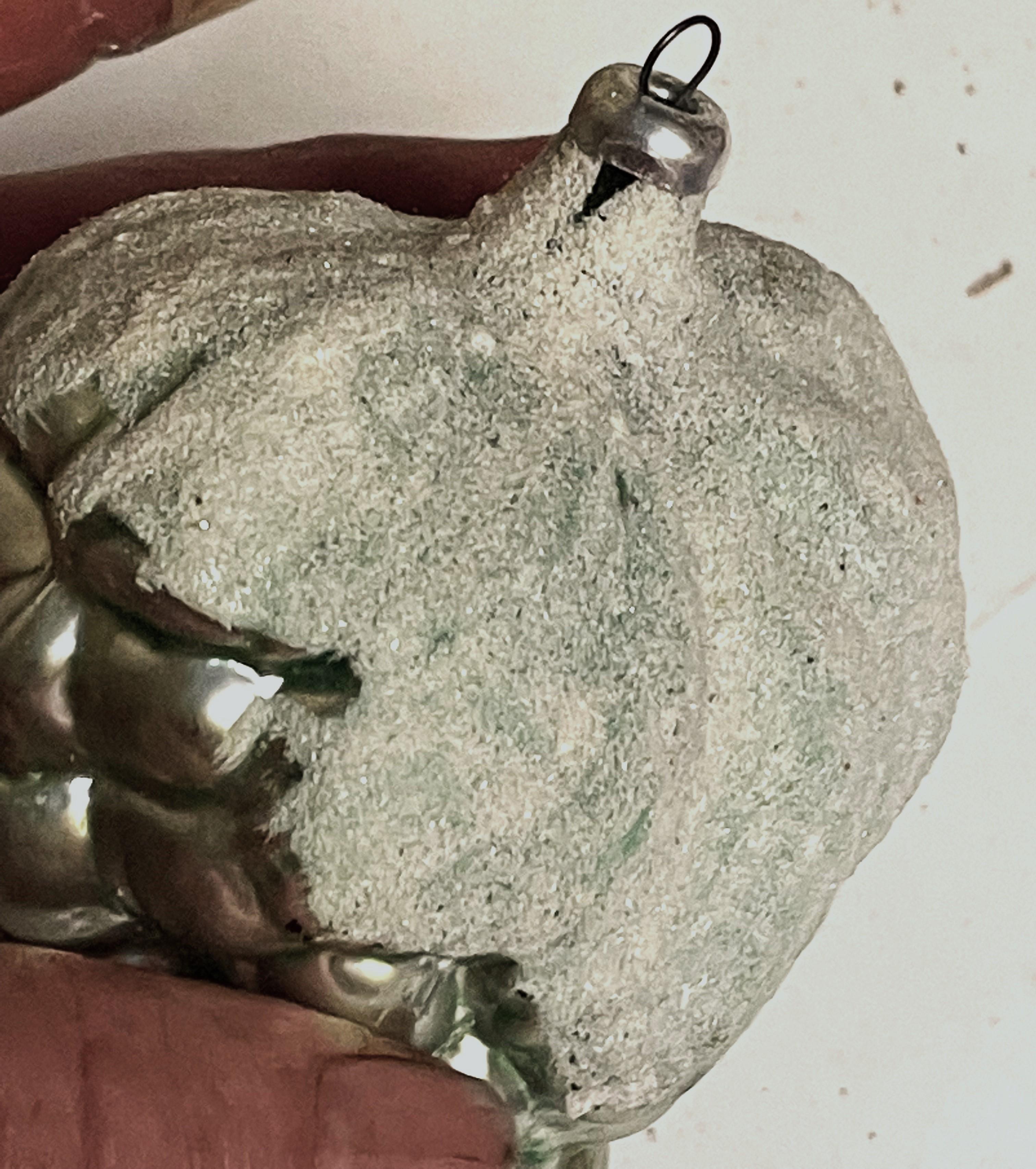 Si tratta di un meraviglioso ornamento natalizio di grandi dimensioni in vetro mercurio soffiato a mano a forma di grappolo d'uva. Gli acini sono di colore argento con una foglia su ogni lato che ha una finitura zuccherina che sembra neve. 

Non ci