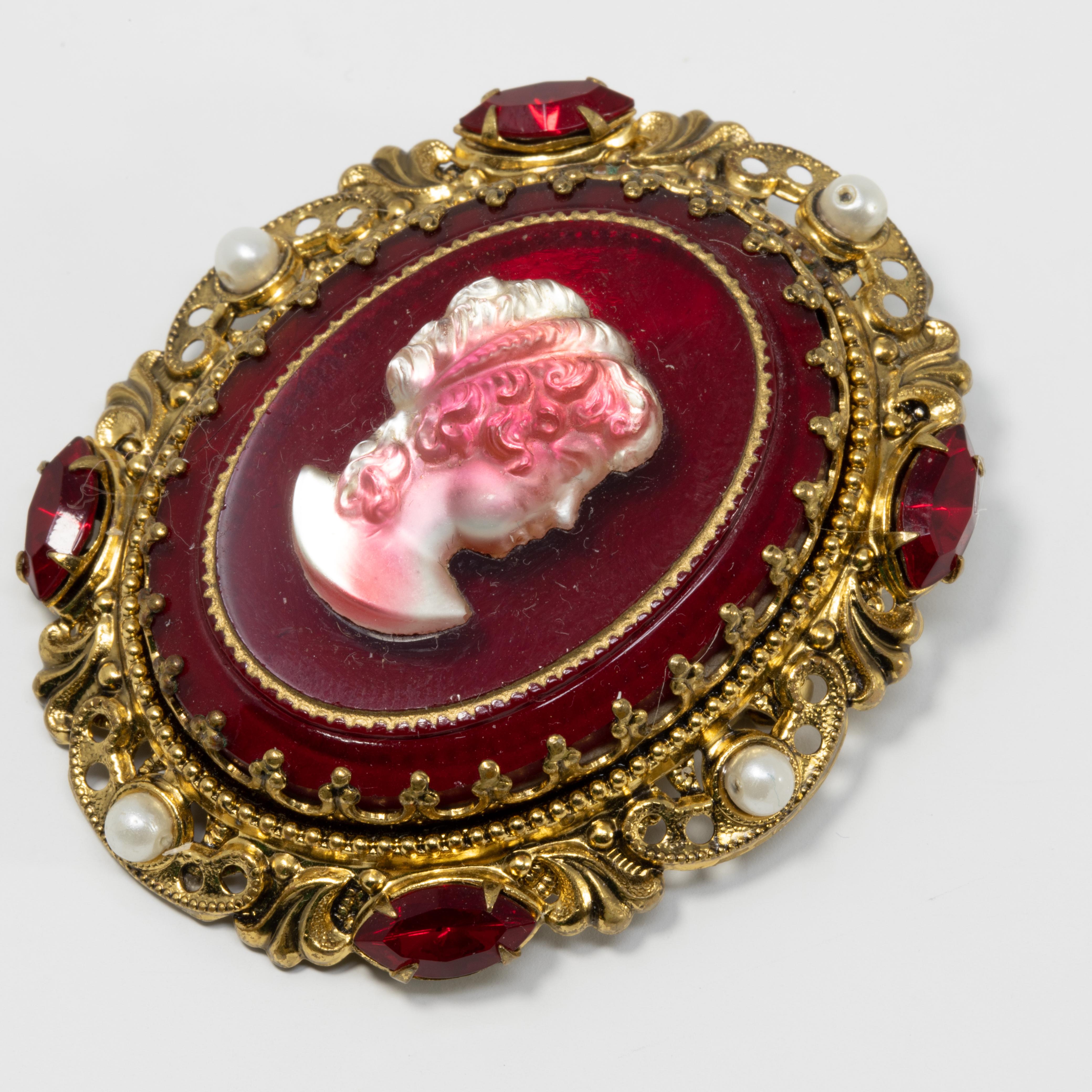 A gorgeous German demi parure featuring a pair of ornate clip on earrings and a matching pin/brooch. Each features a red and white glass cameo prong set in an ornate Victorian setting. The setting is accented with faux pearls and red crystals.