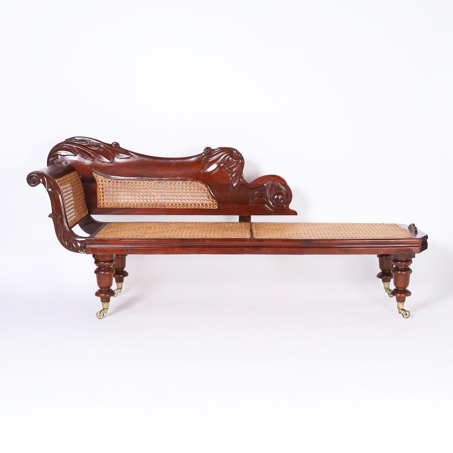 British colonial daybed, most likely Barbadian crafted in mahogany with a graceful form, floral carvings, handmade construction, caned seat, back and side, and turned legs with brass casters.