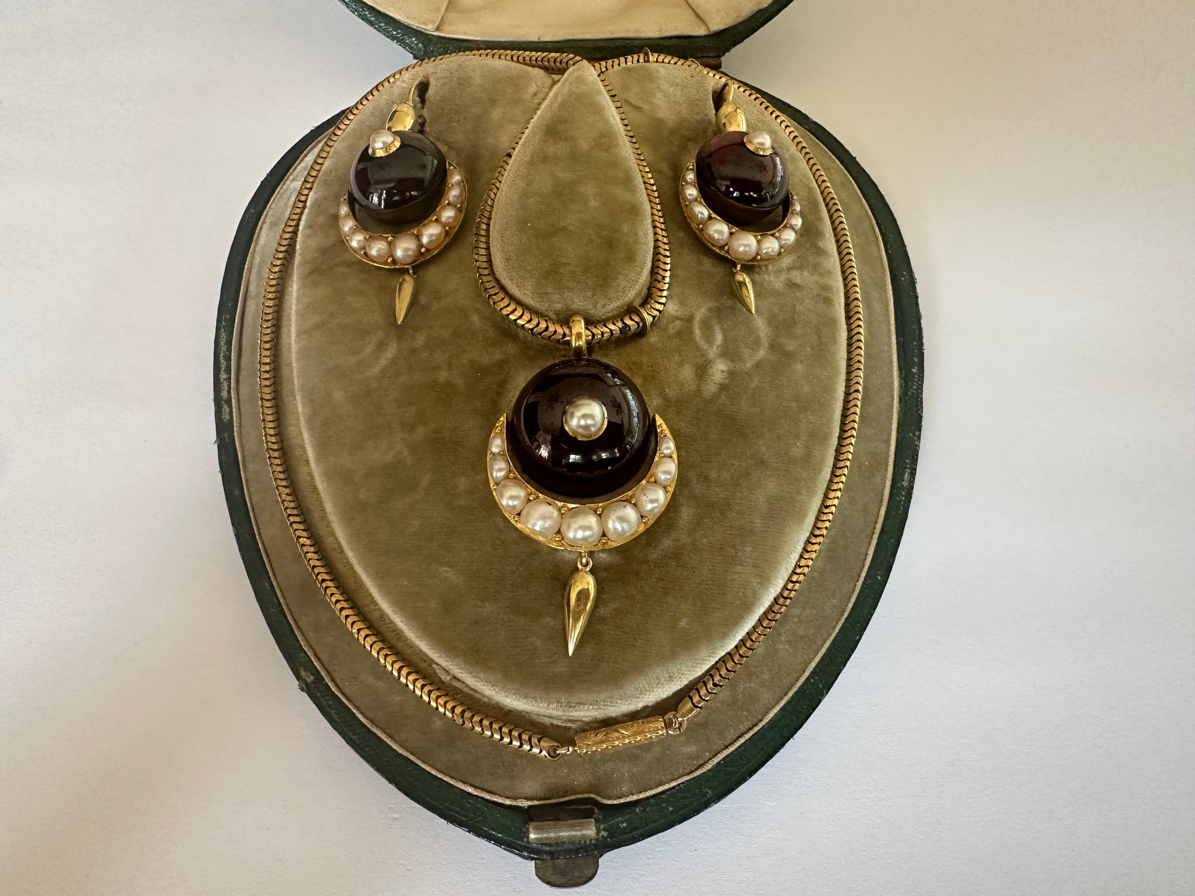 Questa suite vittoriana comprende una collana pendente e un paio di orecchini pendenti abbinati, ciascuno dei quali reca un granato cabochon rosso di grandi dimensioni accentuato da mezzelune composte da nove perle naturali scintillanti con