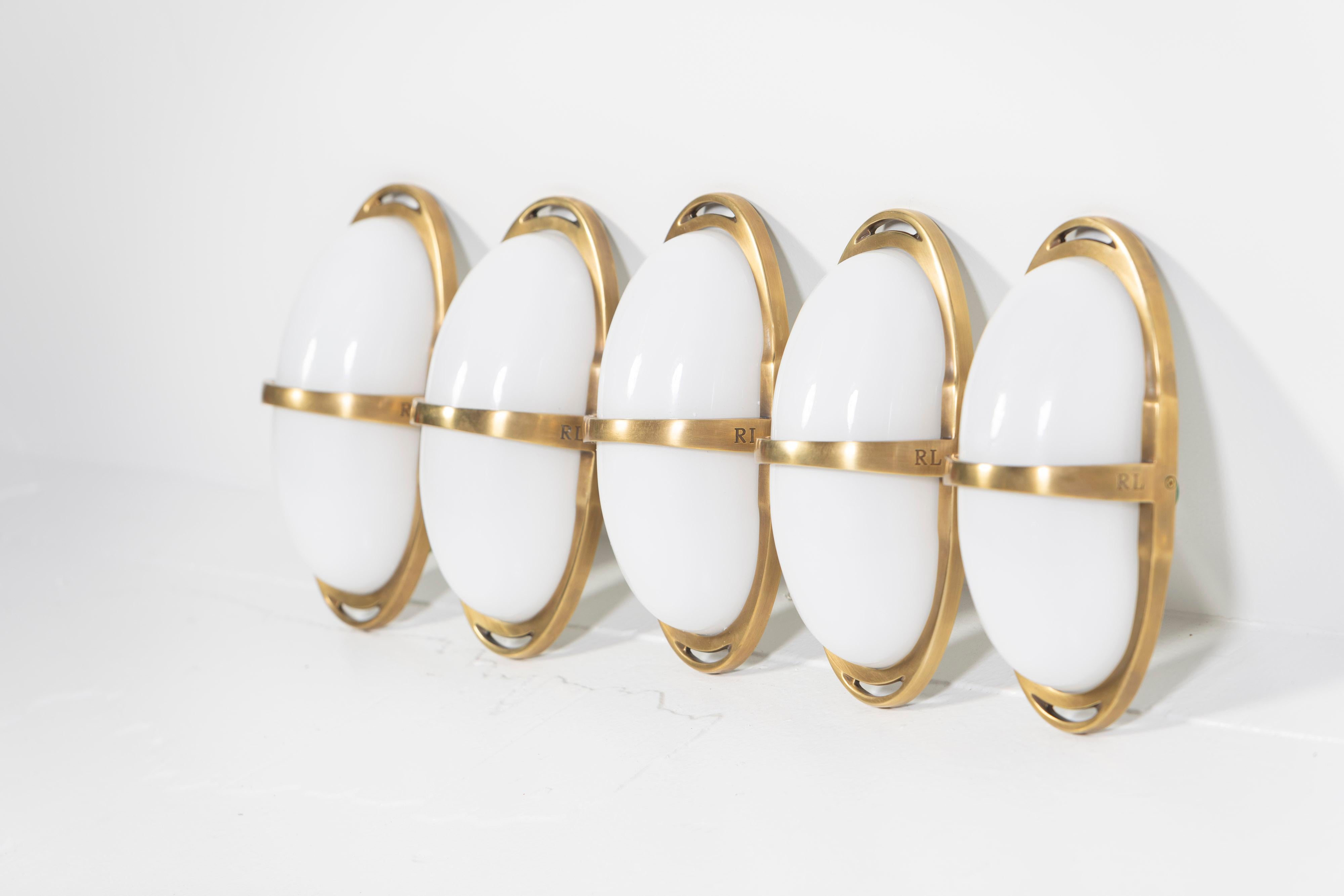 Two pre-owned Westbury Double Sconces, designed by Ralph Lauren Home for Visual Comfort are in natural brass with white glass. This double sconce features a sleek demilune glass shade offset by open brass framework. Perfectly situated for dining
