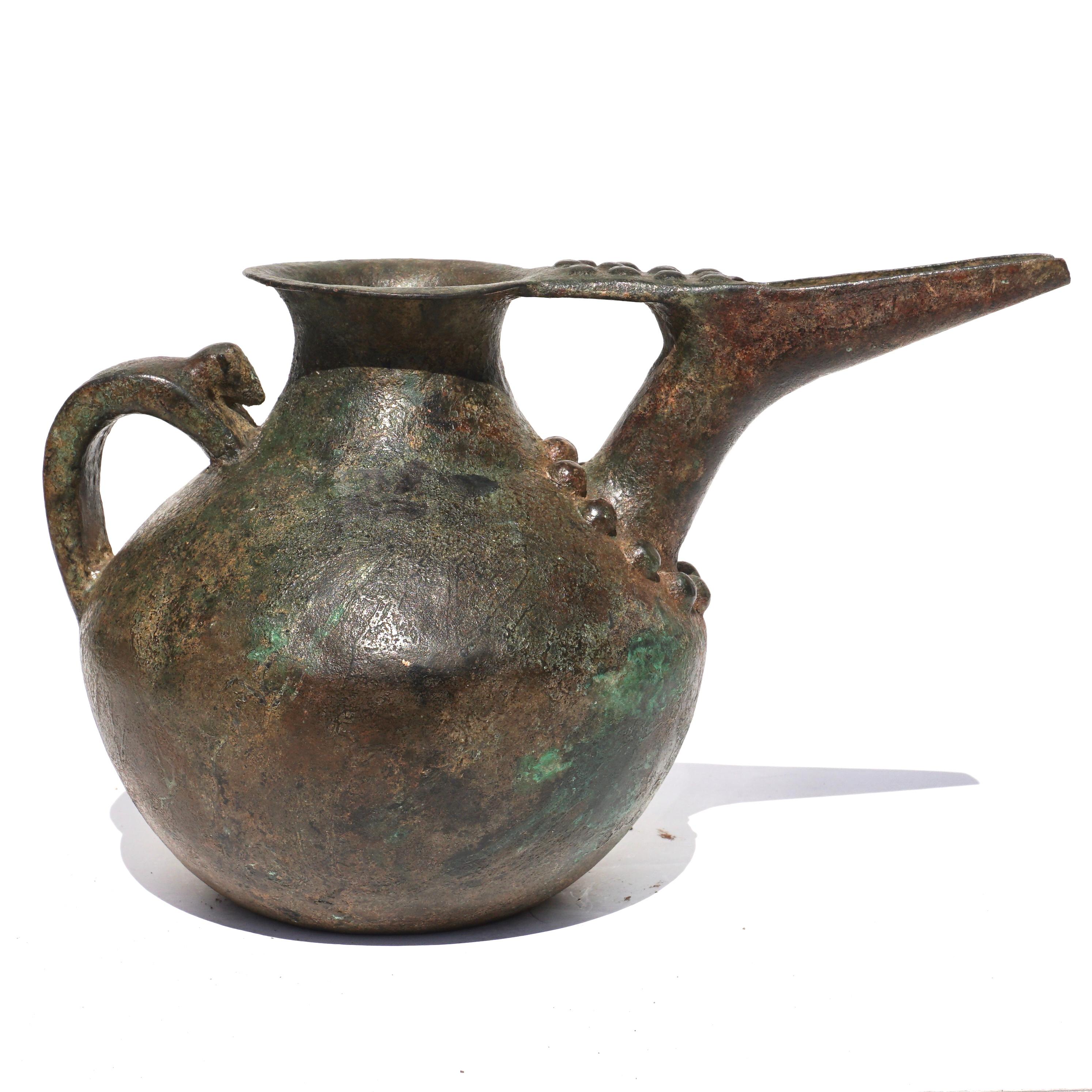 c. 1100- 7th century BC. Western Asiatic. 

Large bulbous bronze vessel with flat base and a long spout. Decorated with hemispherical rivets encircling the base of the spout where it is attached to the vessel and on top of the spout. A ram or mouse