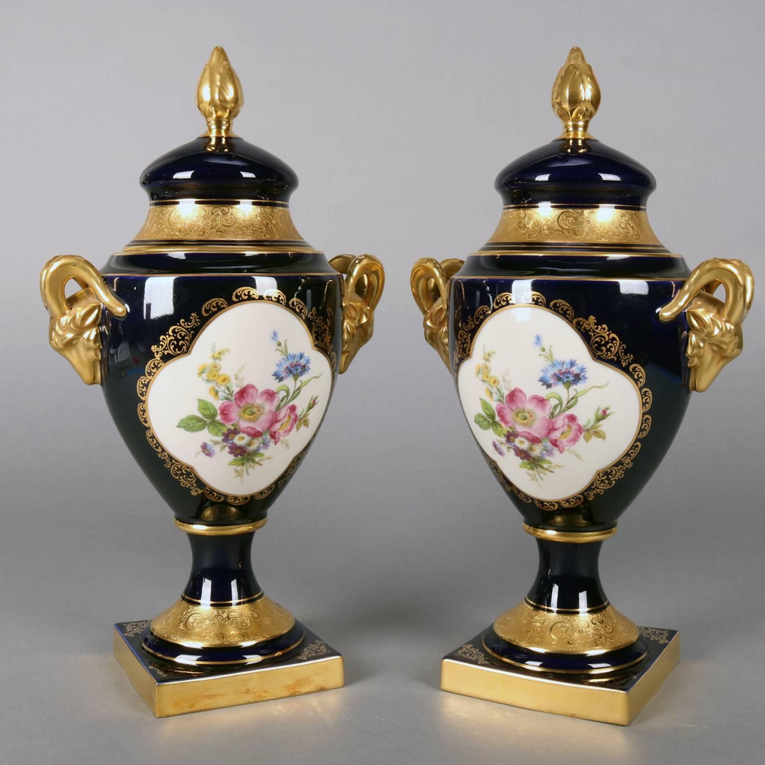 Urnes en porcelaine de l'école de Meissen d'Allemagne de l'Ouest présentant des réserves florales peintes à la main sur fond bleu cobalt et des rehauts fortement dorés, notamment des poignées en forme de tête de bélier, avec au verso 