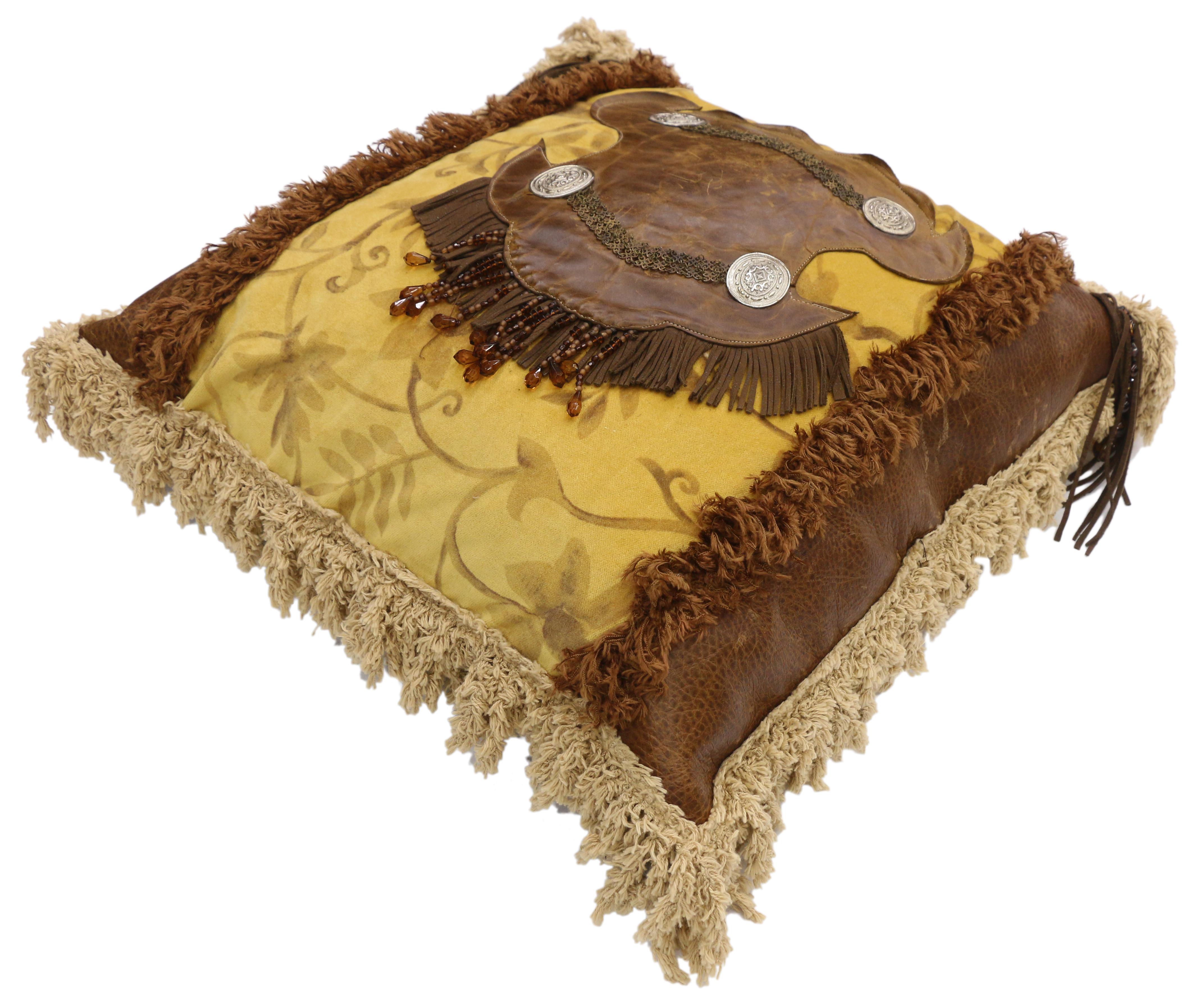 Western Rockabilly style leather throw pillow with fringe and tassels. This Western style throw pillow features a golden yellow fabric backdrop with a leather centerpiece adorned metal accents, fringe, and beads. The golden yellow center is flanked