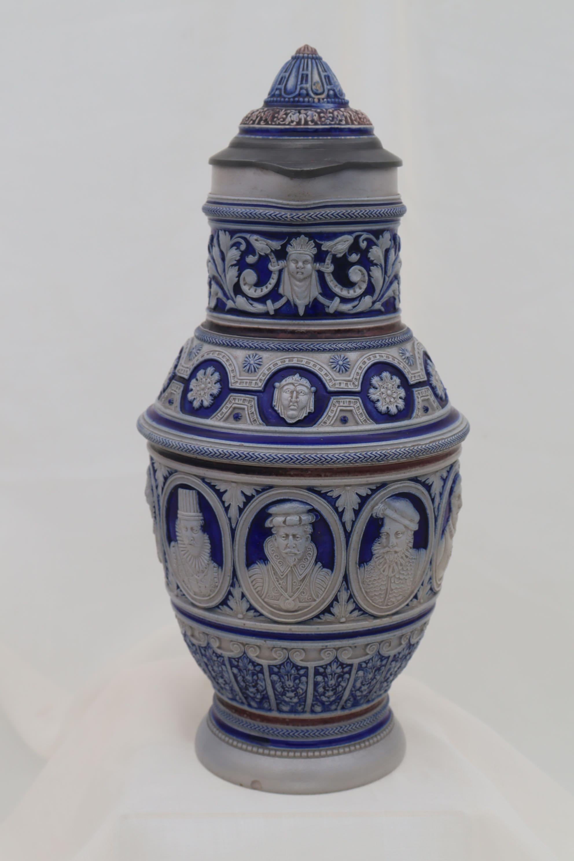 This intricately detailed Westerwald stoneware beer jug is encircled with a central band of portraits of figures in medieval dress, with more decoration above and below. The backgrounds to these decorations are a rich cobalt blue, and the blue with