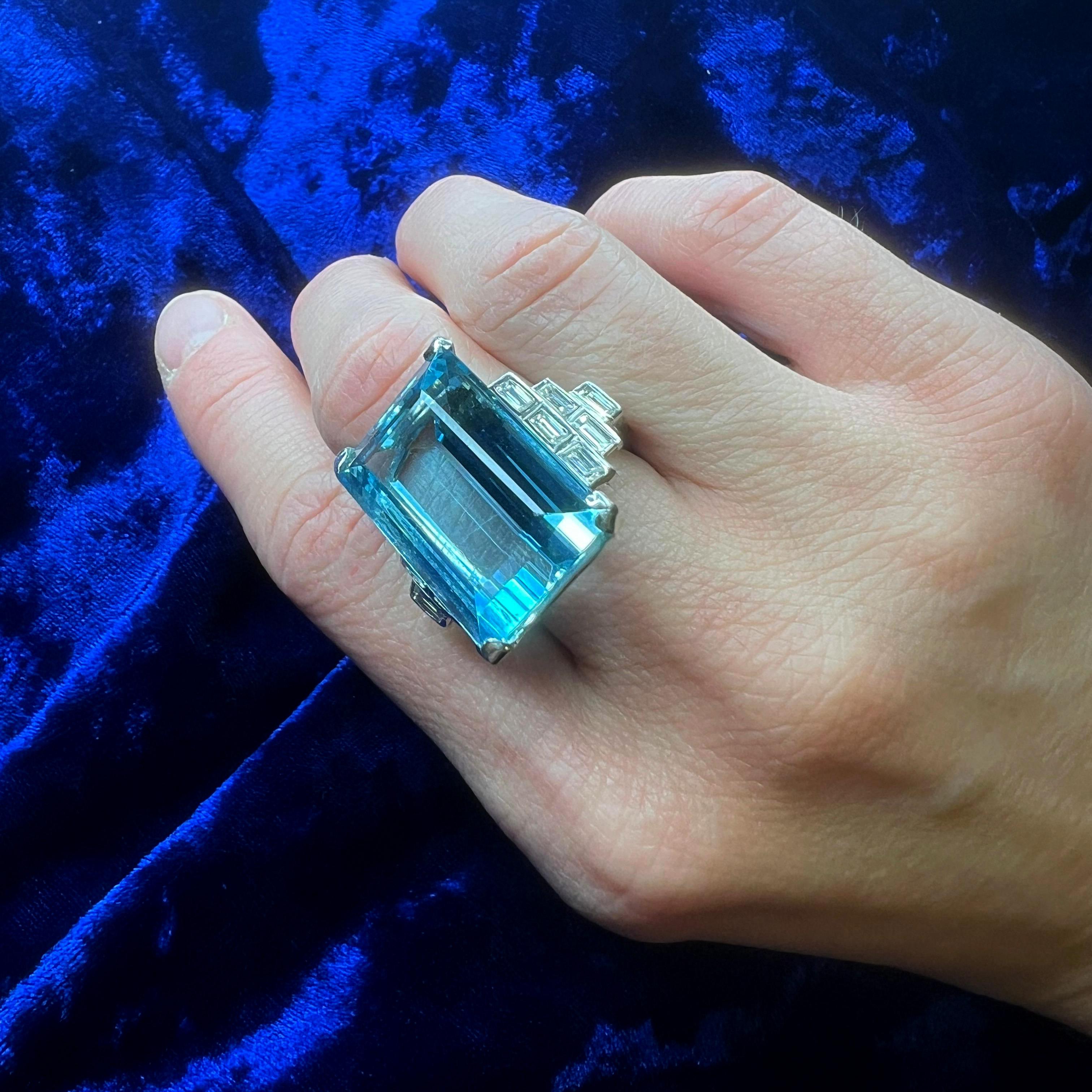 18kt White Gold 23.60 cts. Step-Cut Aquamarine and Diamond Ring. 

An impressive 18kt white gold ring, showcasing a stunning 23.60-carat rectangular step-cut natural aquamarine, accented by twelve baguette-cut diamonds set in a striking geometric