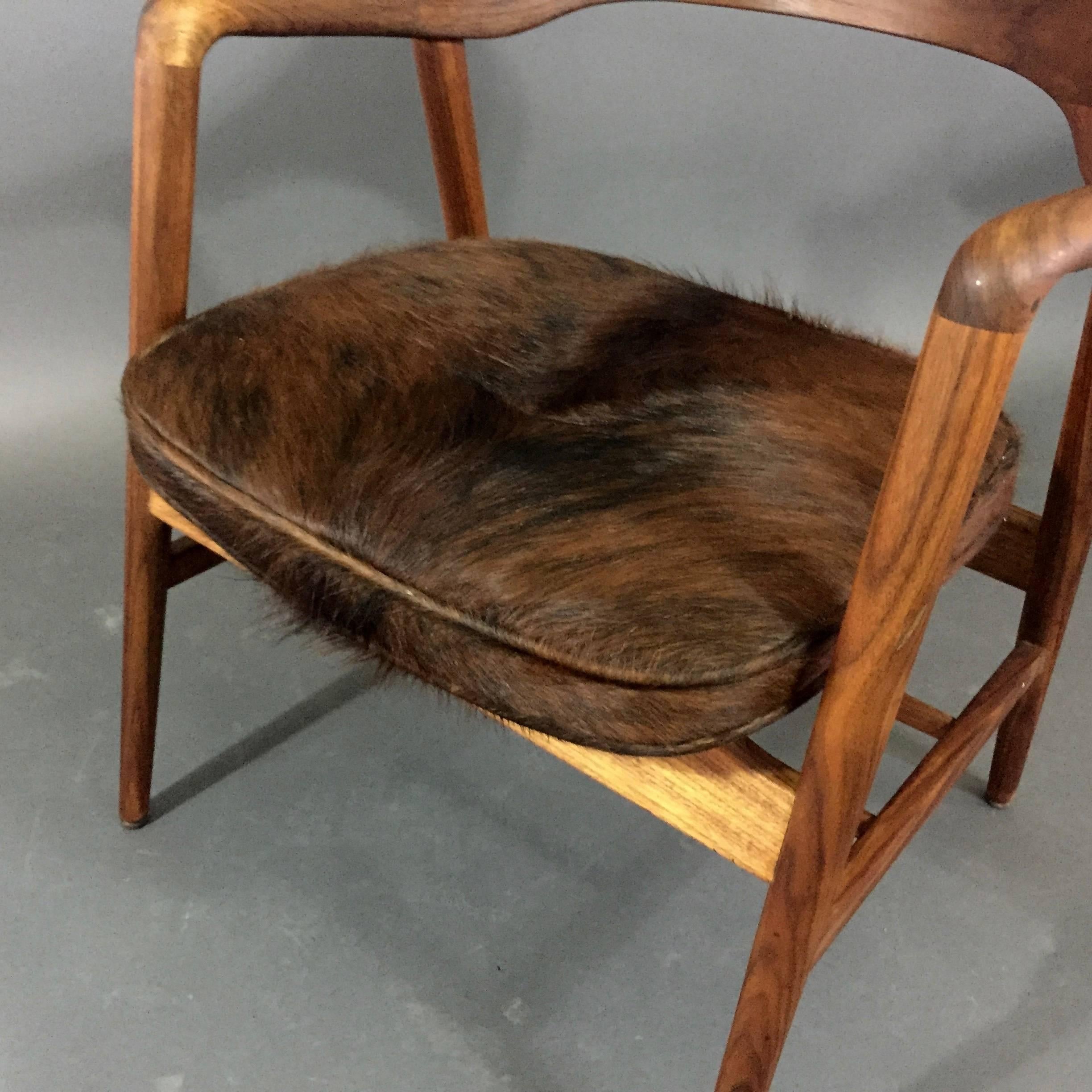 A few versions of this chair have been made as either dining chairs or a desk chair by the Wayland NY based W.H. Gunlocks company. This version is gorgeous solid sculpted walnut with a magazine rack to the underside. Recently upholstered in a luxe