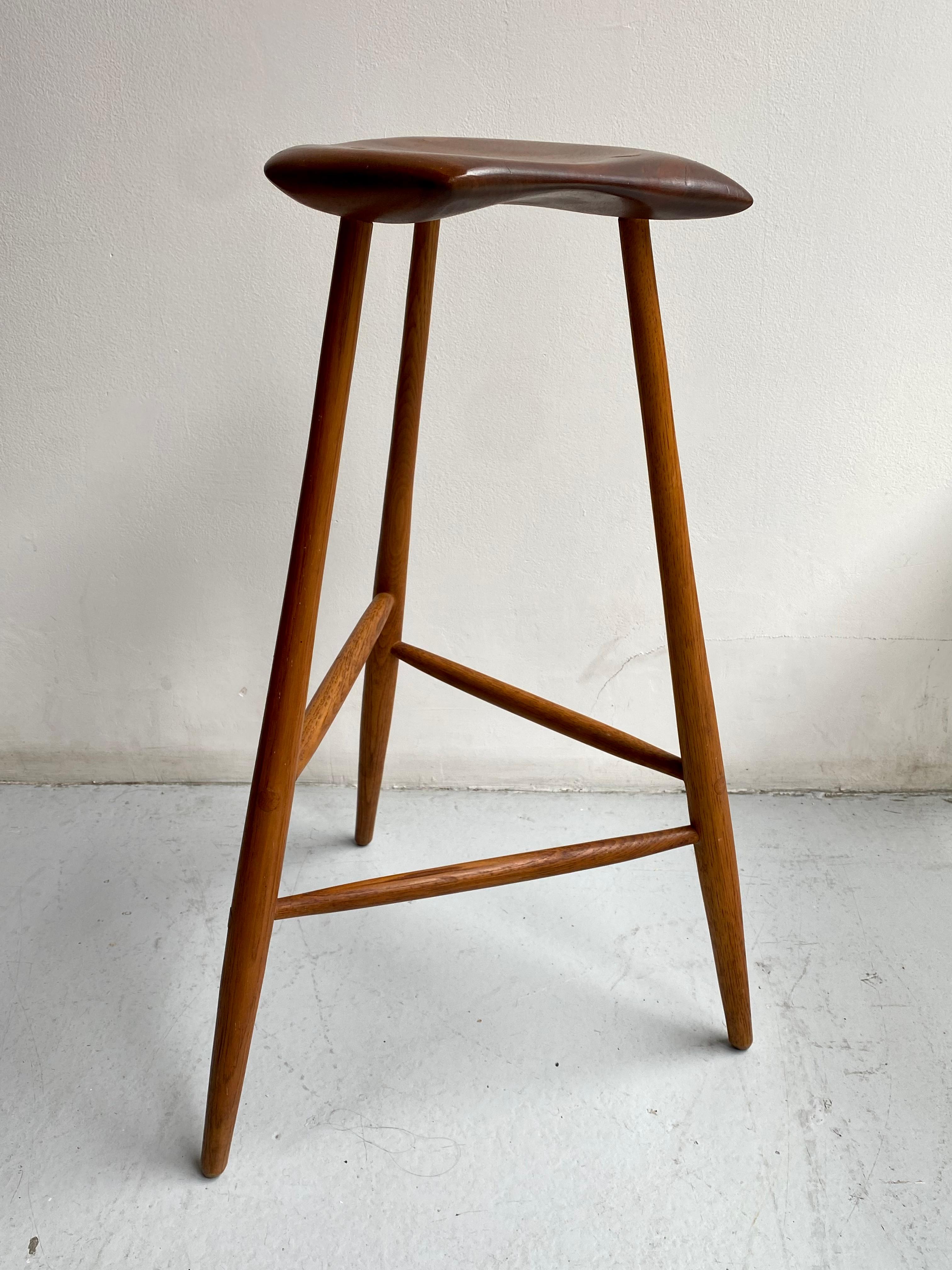 Der 1958 entworfene dreibeinige Hocker von Esherick ist eines seiner bekanntesten Stücke. Da die Form des Sitzes von der Maserung jedes einzelnen Nussbaumholzes abhängt, gleicht kein Exemplar dem anderen. Eingeschnitzte Signatur und Datum auf der