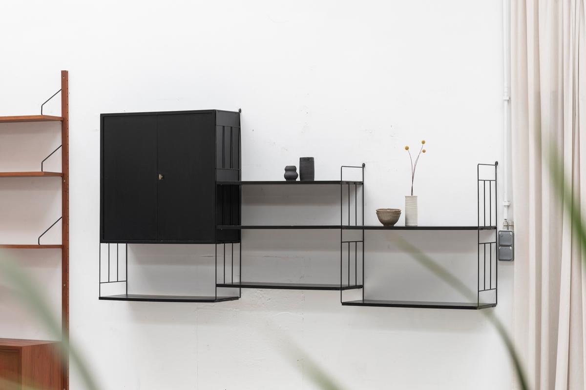 Floating shelving system by WHB, designed and produced in Germany in the 1960s. Metal and black painted wooden design, easy to install and adjust. The system features one cabinet with hinging doors. The 6 shelves rest easily on the metal supports