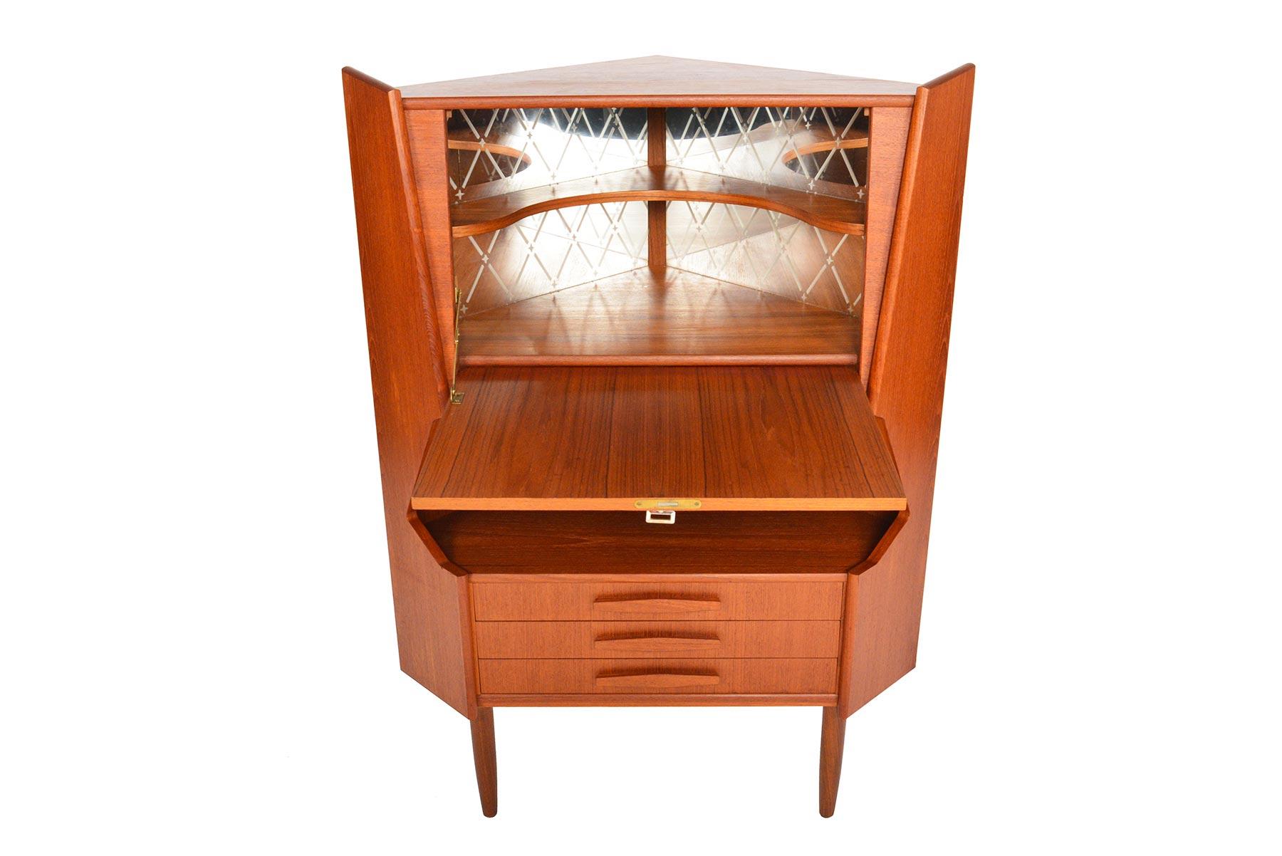 This fabulous Danish modern midcentury corner bar in teak will brighten up any modern home. Beautifully sculpted with atomic stylings, this piece offers a drop down door which opens to an etched mirror lined interior and black laminated shelf. Three