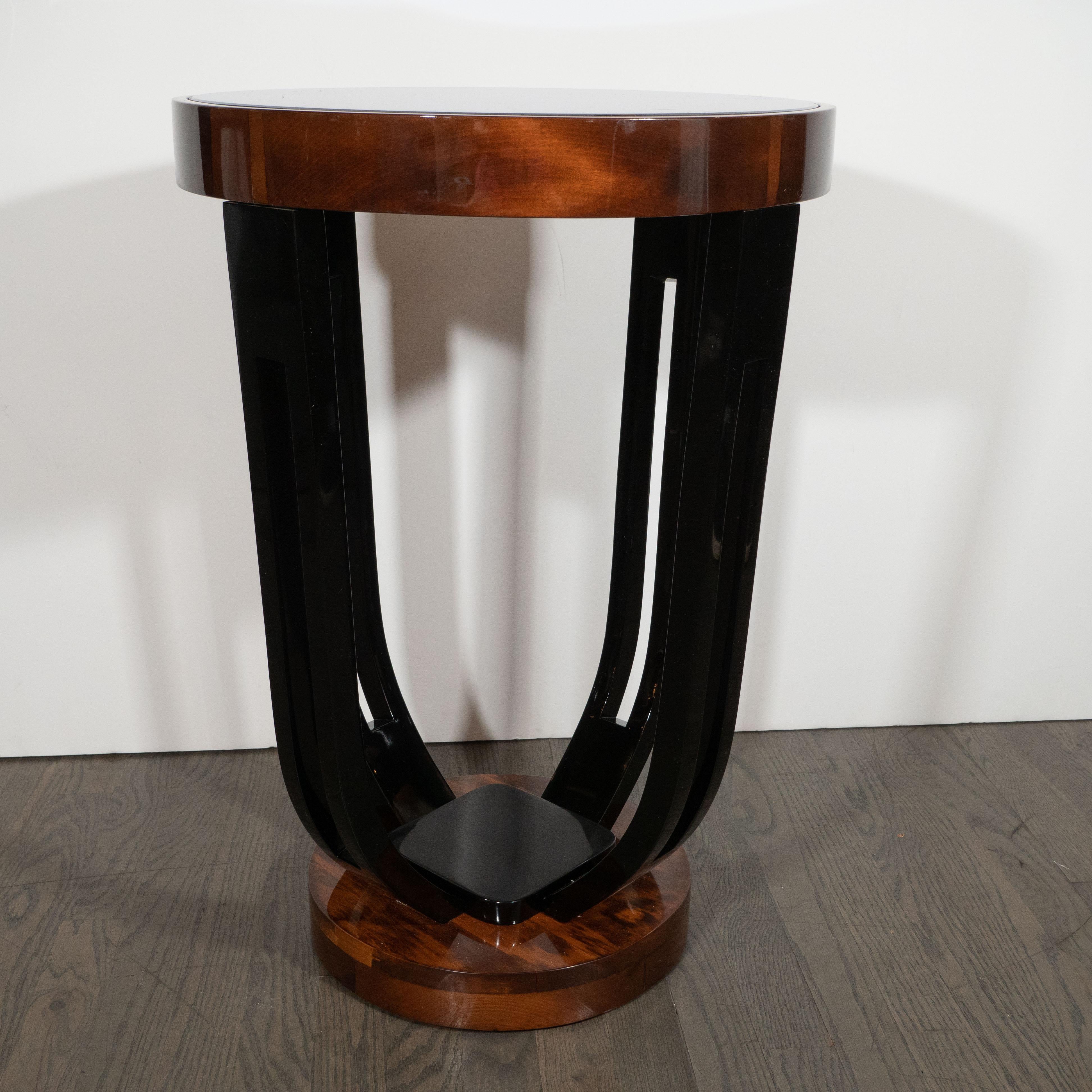 This elegant Art Deco Skyscraper style Machine Age Gueridon table was realized in the United States circa 1935. It features four streamlined black lacquer supports with rectangular cut outs that attach to a circular black mirror top wrapped in