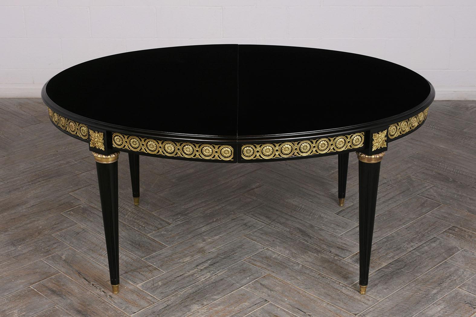 This 1930s French Louis XVI style dining table is made of mahogany wood ebonized in a rich black color with a lacquered finish. The oval shaped table is elegantly adorned with brass accents along the edge. The carved legs feature fluted details and