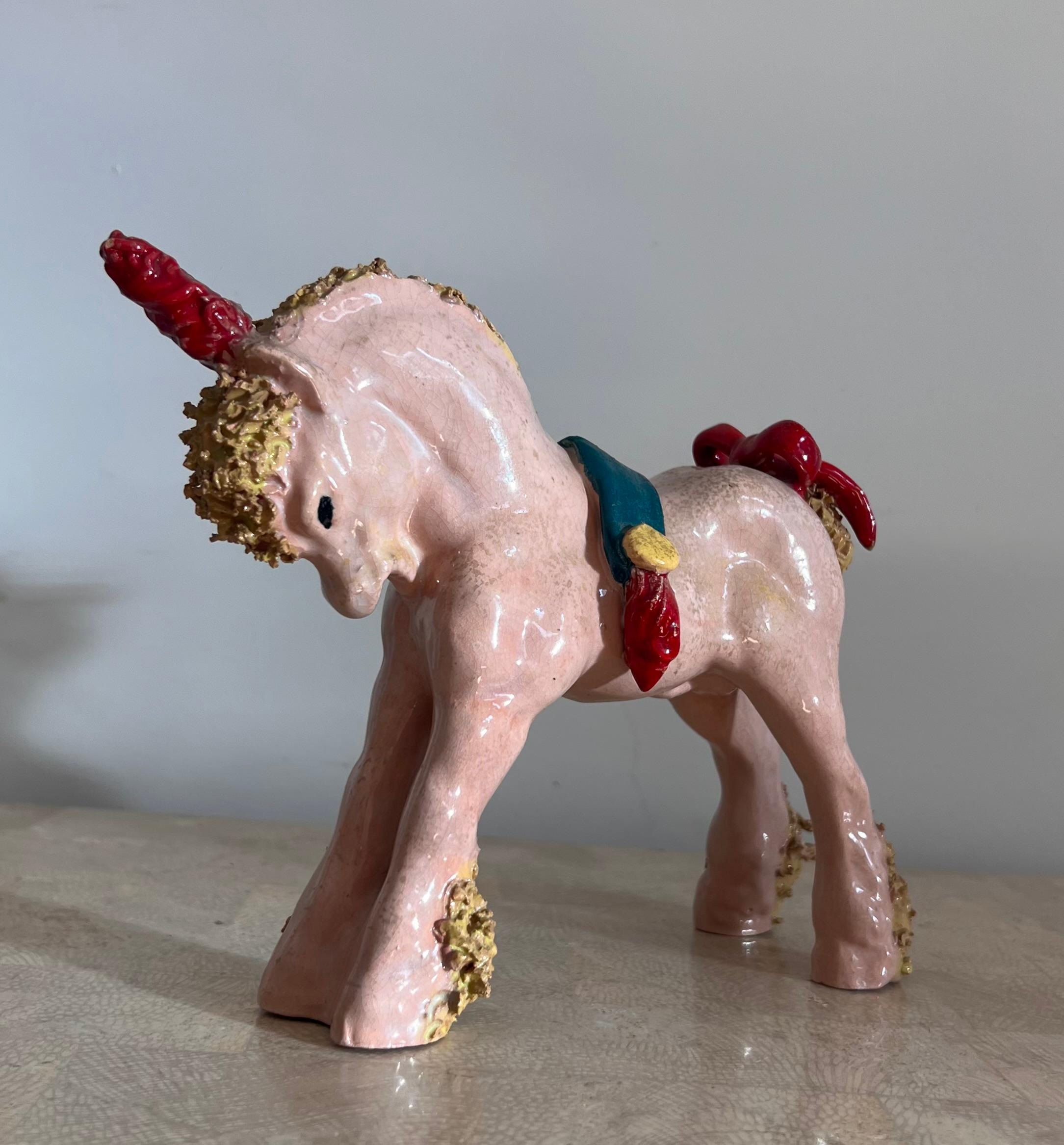 A whimsical little statue of a pony unicorn by Bill Meyer, signed, 20th century. Pale pink with pastel chartreuse hair and hooves, teal saddle with marigold accents, and brick red ribbons and horn. Signed on bottom voice. A lovely memento of the