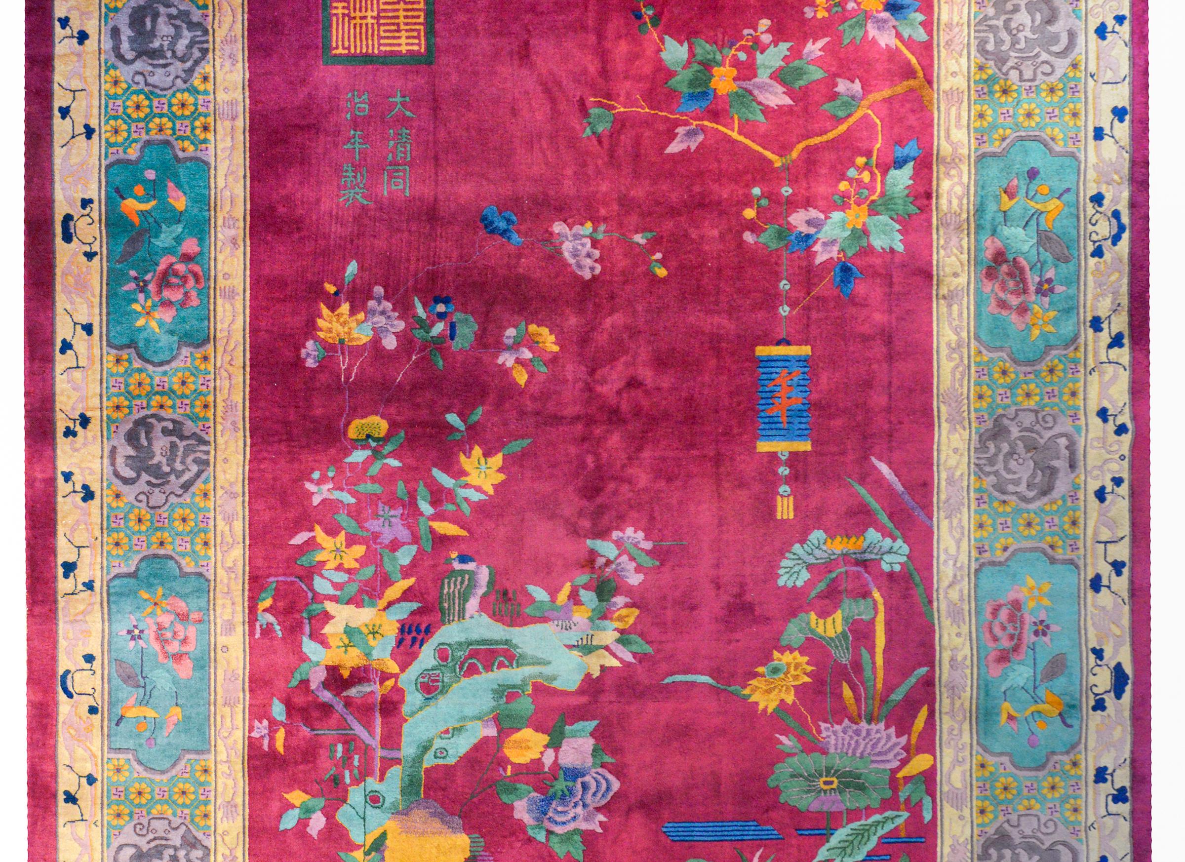 A whimsical early 20th century Chinese Art Deco rug with a peaceful garden landscape depicting a flowering tree branch with a lantern hanging over the corner of a pond with blossoming lotus and scholar's rocks, all on a bright cranberry background