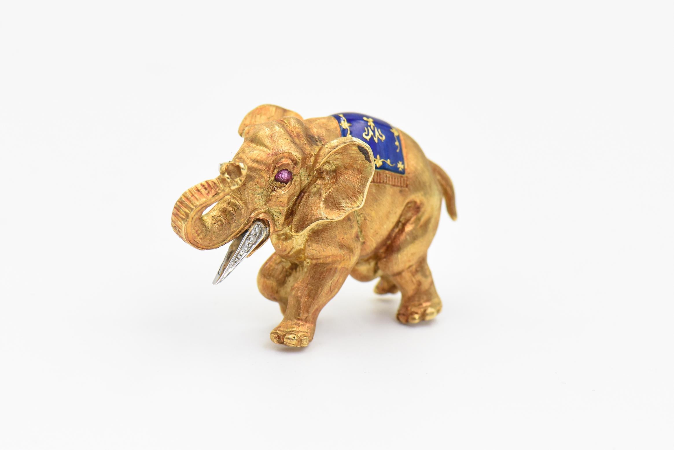 Whimsical three dimensional walking (strutting) elephant brooch made of 18k yellow gold. Highly stylized so you can see the creases around his legs and the wrinkles in his trunk. - a piece of art.  This adorable elephant has a diamond tusk, ruby eye