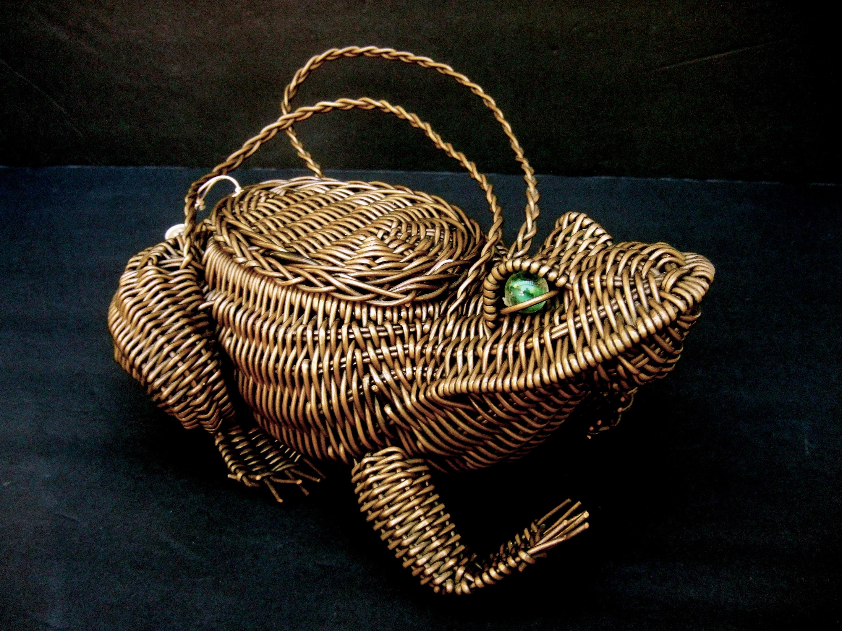 Whimsical figural wicker frog design handbag c 1960s 
The quirky handmade artisan handbag is designed in the shape
of an endearing frog 

Adorned with a pair of green glass marble eyes. Carried with a pair
of matching woven wicker handle straps. The