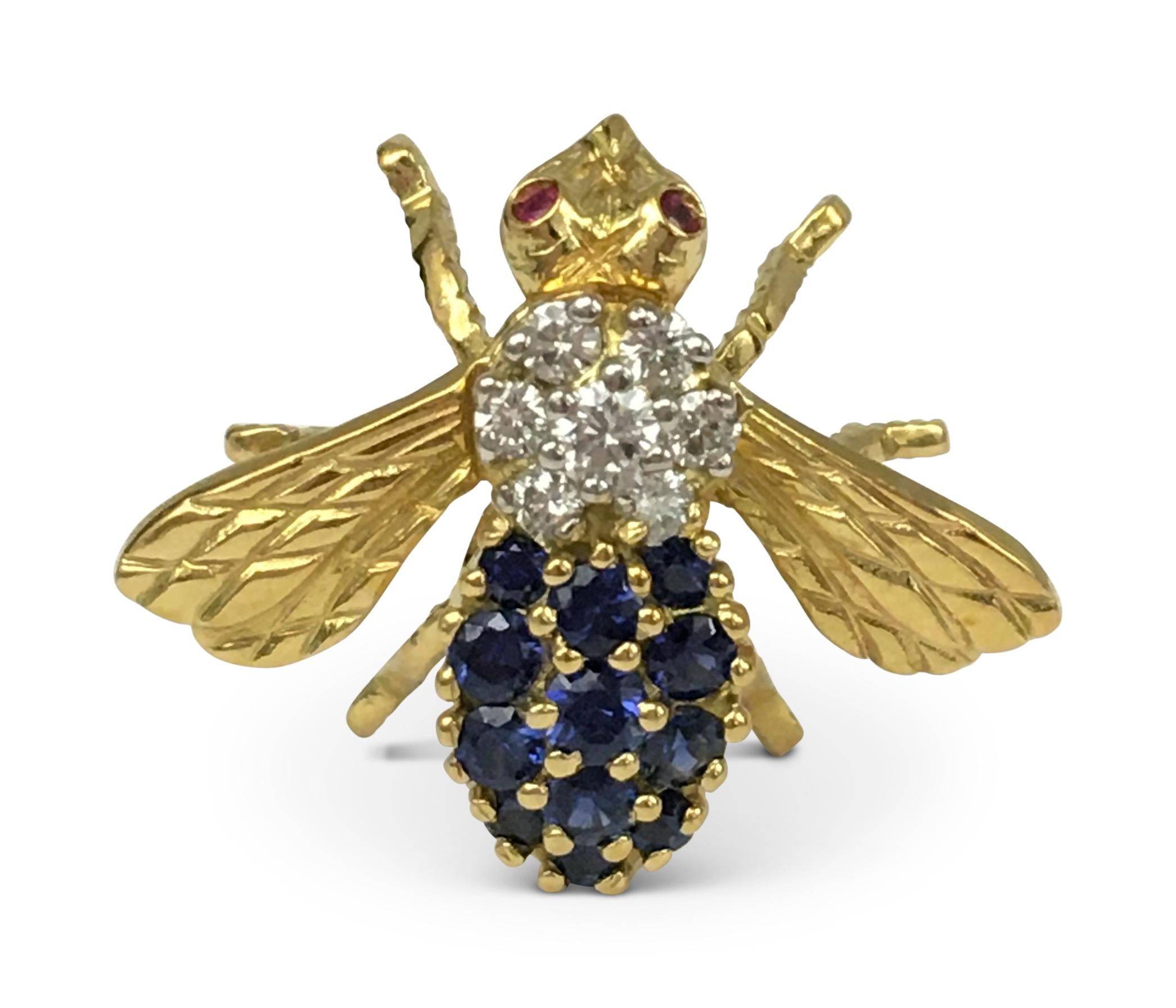 Whimsical bumble bee pin is set with high quality round brilliant cut diamonds (approx. 0.25 cttw, E-F color, VS clarity) and well matched blue sapphires (0.35 cttw) on the body. The bee is completed with ruby stone eyes. Measures 23mm x 27mm. The